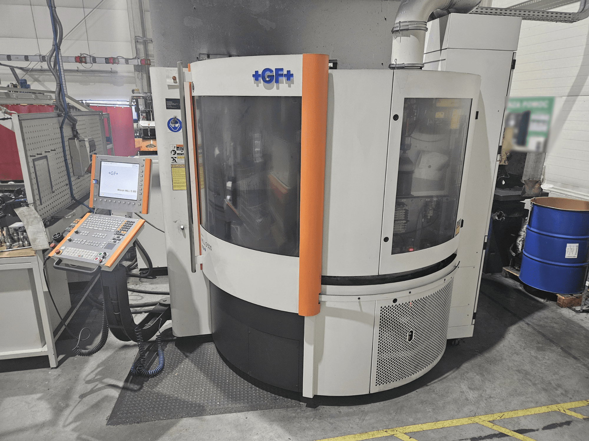 Obrabiarka GF Machining Solutions z panelem sterowania, widok z przodu; przezroczysty panel, pomarańczowe akcenty i przemysłowe ustawienie.