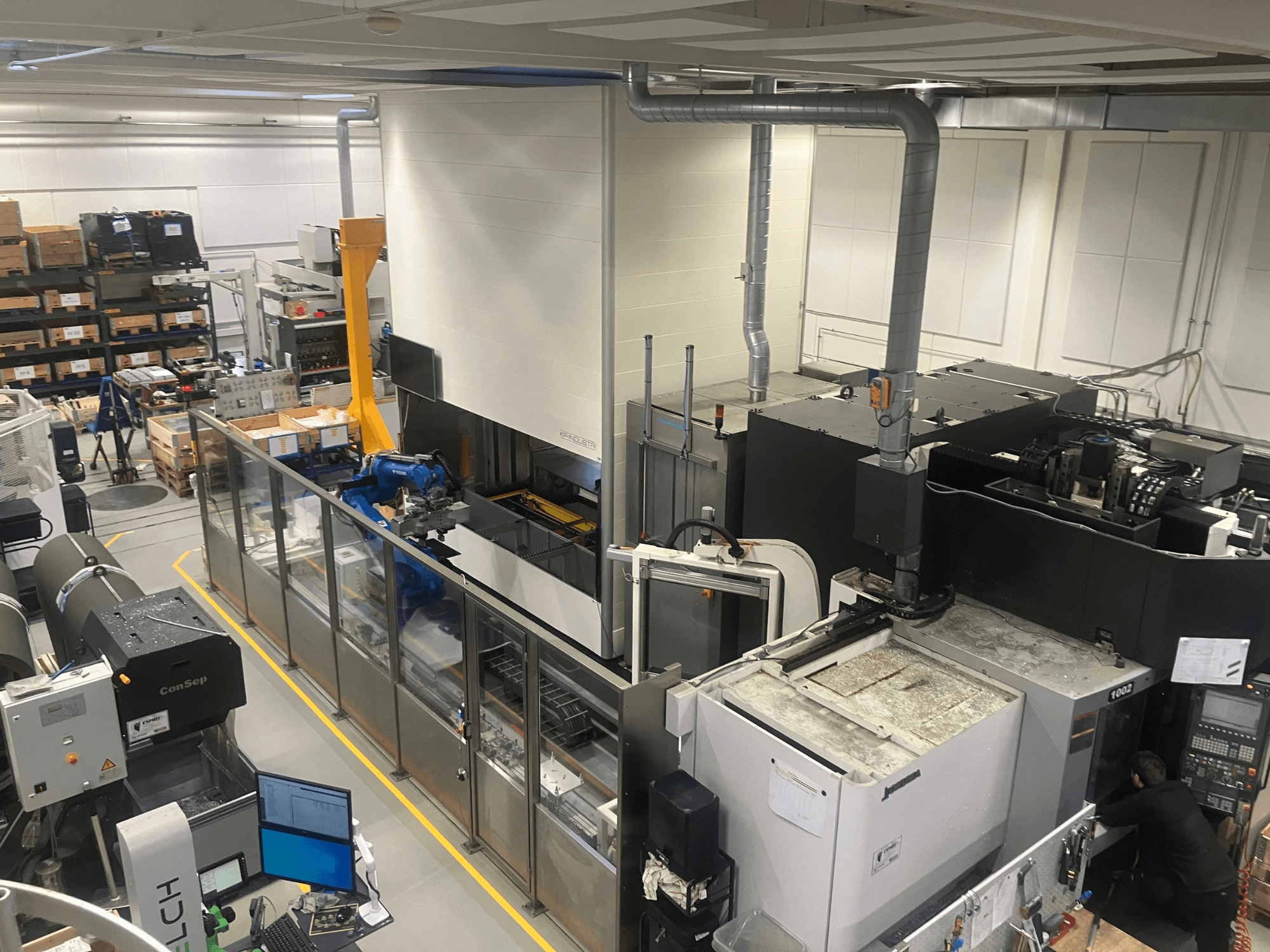 System automatyzacji SSI SCHAFER Logimat w magazynie, widok z przodu; zawiera ramię robota, regały magazynowe i maszyny.