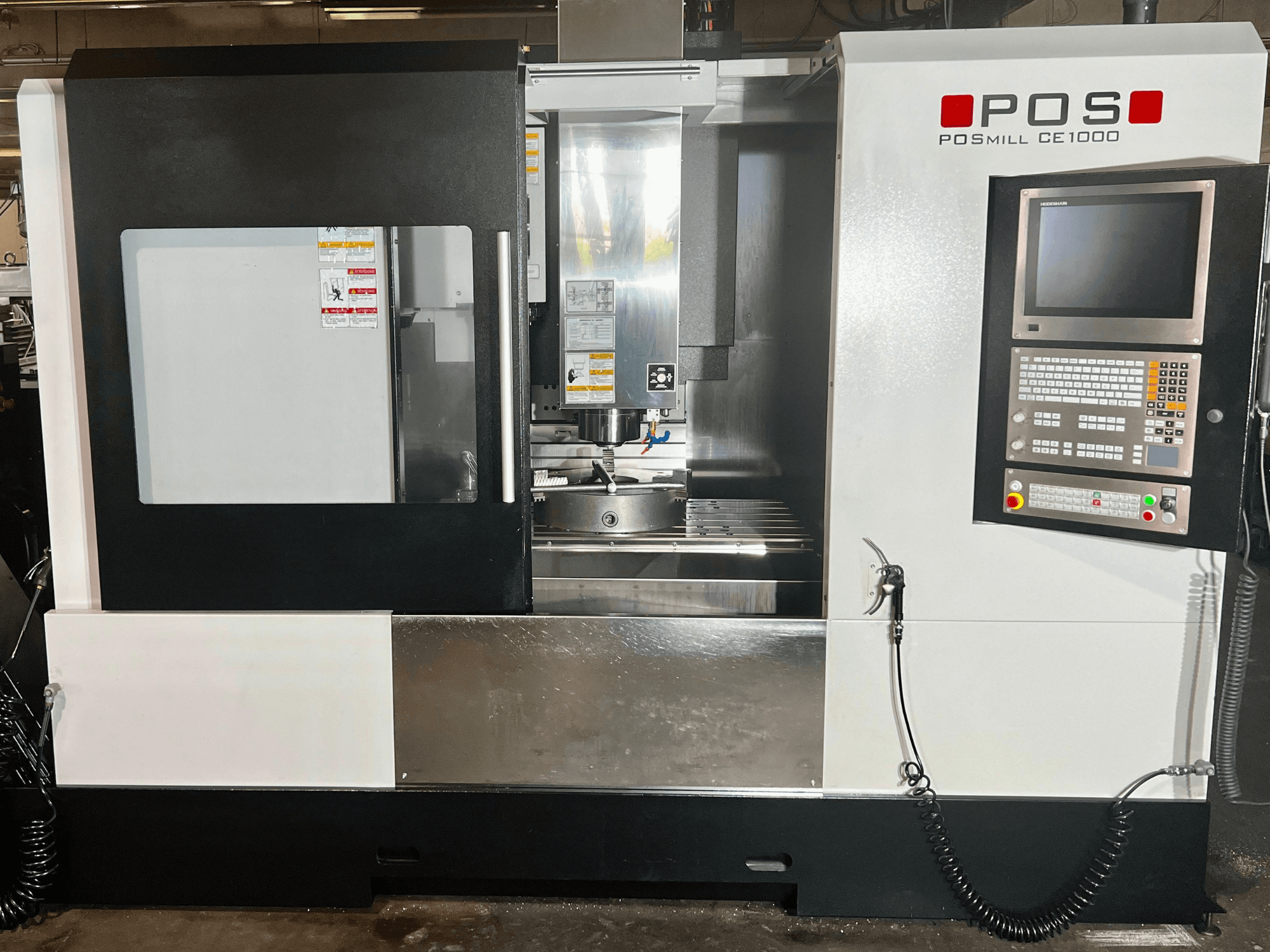 Widok z przodu pionowego centrum obróbczego POSmill CE1000, na którym widoczny jest panel sterowania, okno oraz metalowe powierzchnie.