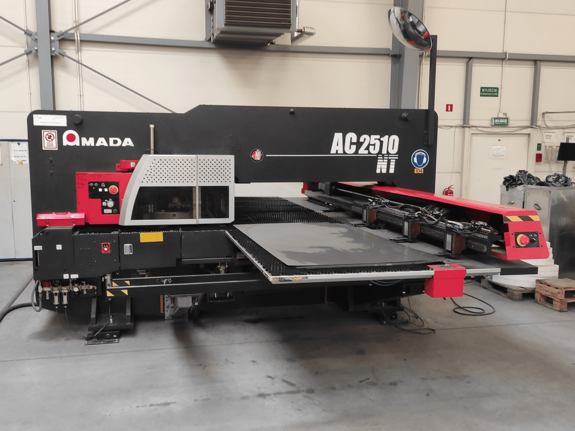 Wykrawarka CNC Amada AC2510 NT, widok z przodu, z panelem sterowania i obszarem ładowania arkuszy.