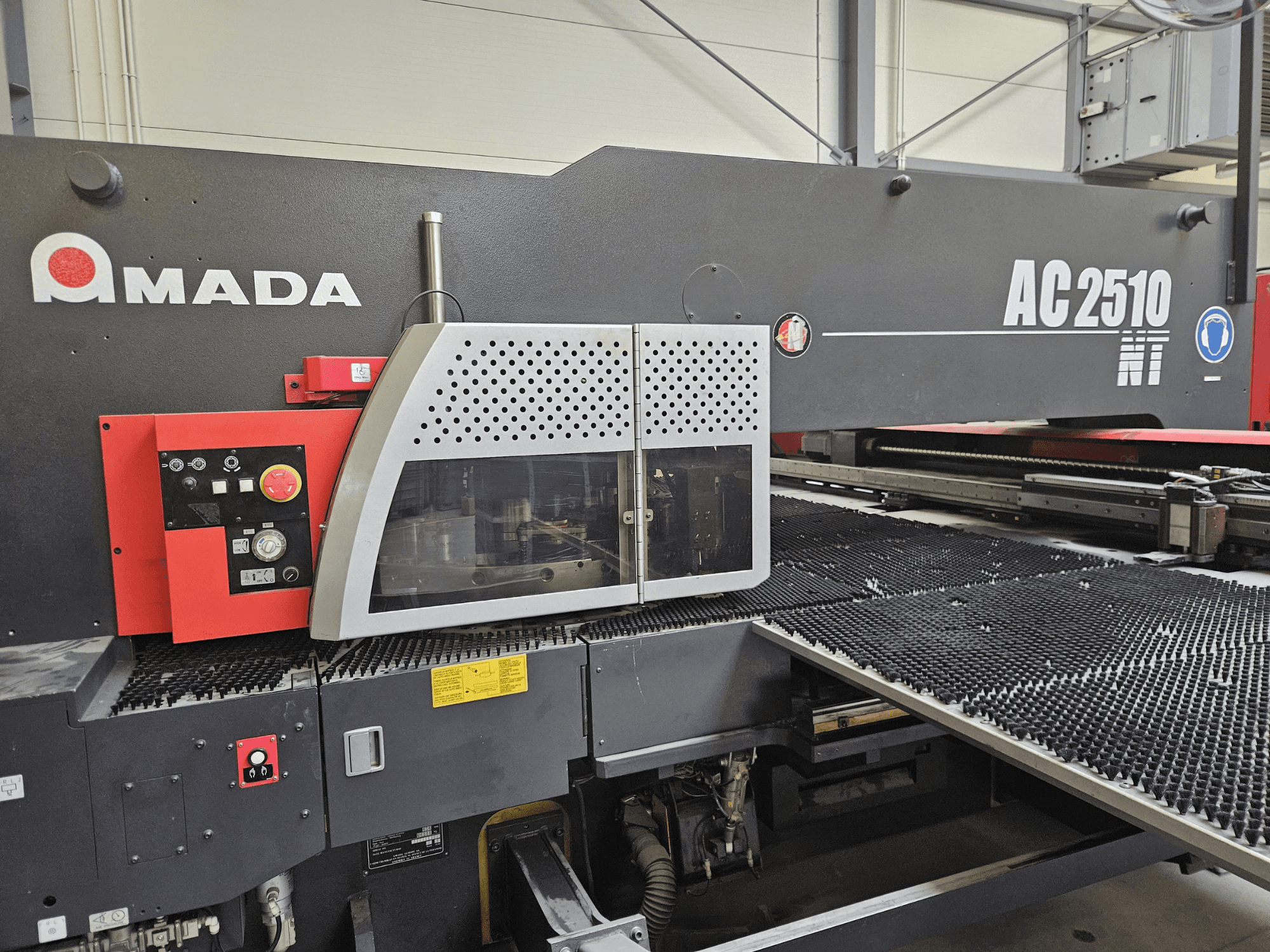 Wycinarka laserowa Amada AC2510 NT, widok z przodu, z panelem sterowania z pokrętłami, przyciskami i osłoną bezpieczeństwa.