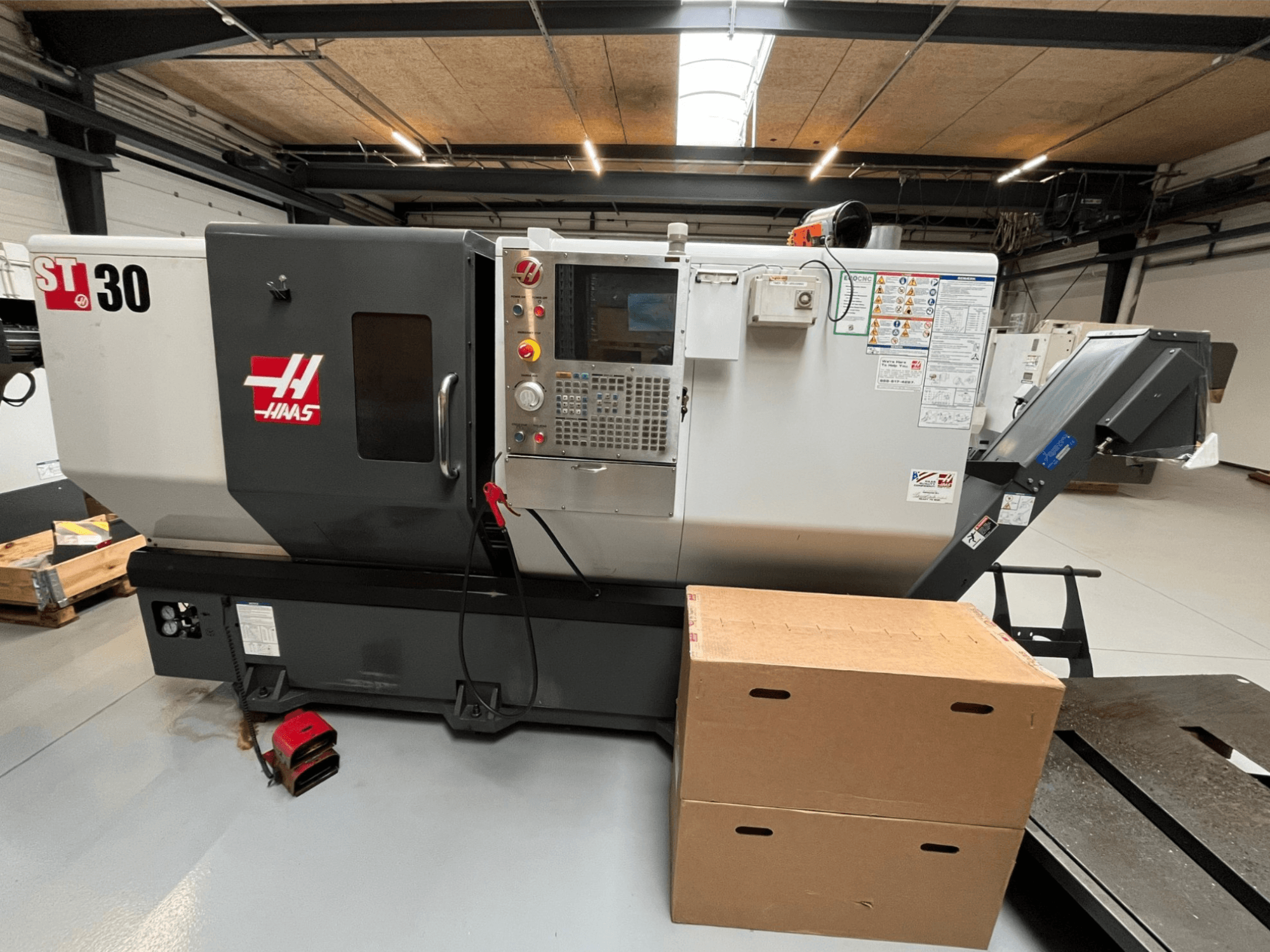 Tokarka CNC Haas ST-30, widok z przodu, panel sterowania z przyciskami, wyłącznik awaryjny i dwa ułożone w stos kartony.