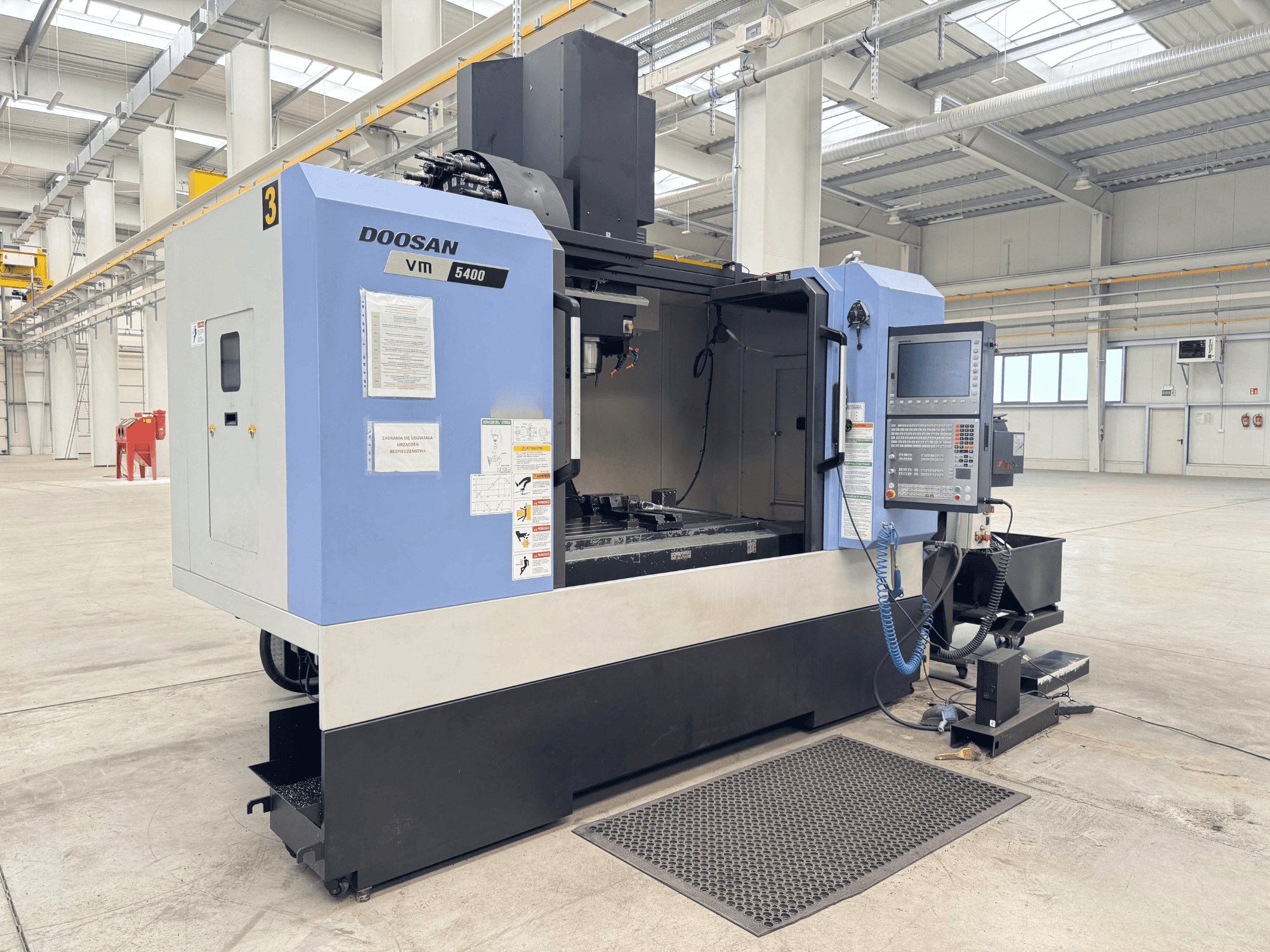 Pionowe centrum obróbcze DOOSAN VM 5400, widok z przodu przedstawiający panel sterowania i obszar roboczy w przestronnym otoczeniu przemysłowym.