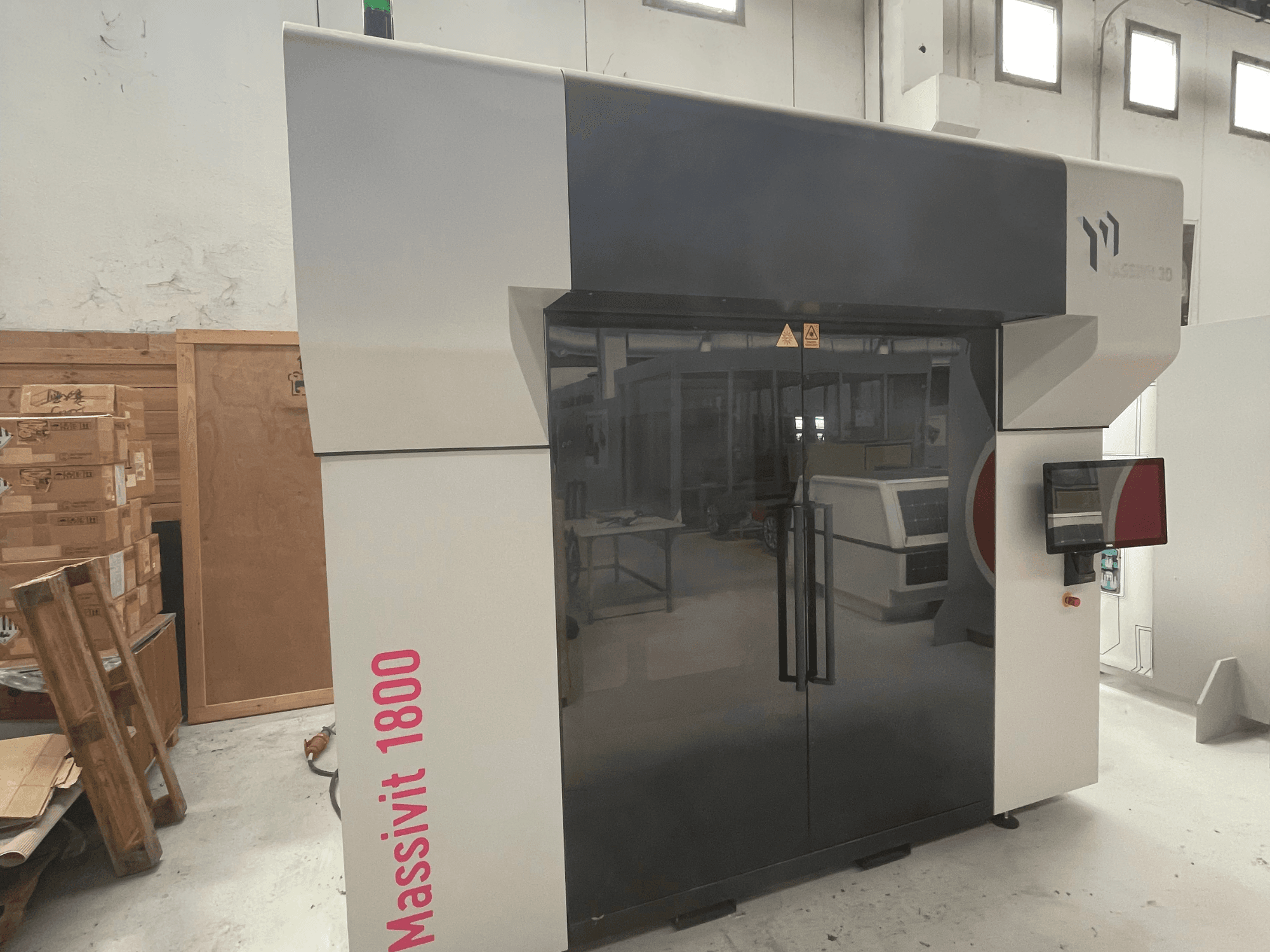 MASSIVIT – drukarka 3D do tworzyw sztucznych Massivit 1800 przedstawiona w widoku z boku, wyposażona w ekran dotykowy i charakteryzująca się eleganckim czarno-białym wyglądem.