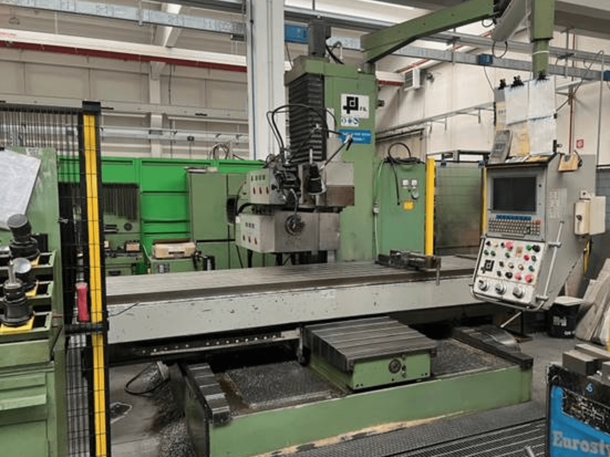 Frezarka przemysłowa firmy JFL, widok z przodu z panelem sterowania, dużym płaskim stołem i wiórami metalowymi na podłodze.