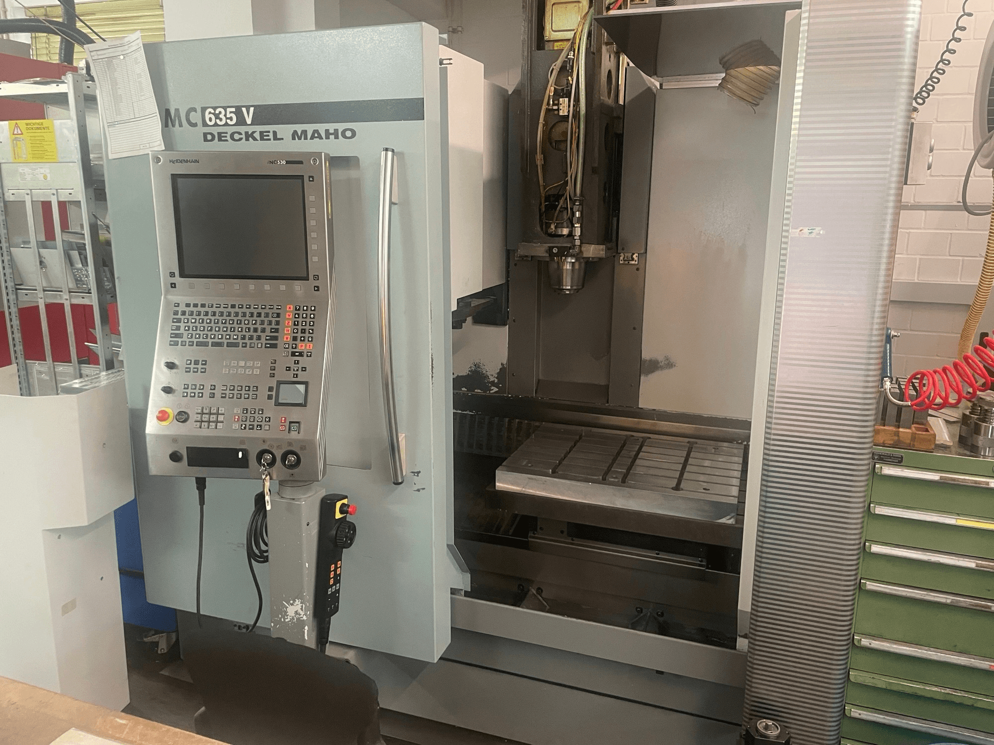 Widok z przodu pionowego centrum obróbczego DECKEL MAHO DMC 635 V z panelem sterowania i otwartą przestrzenią roboczą, przedstawiający głowicę narzędziową i łoże.