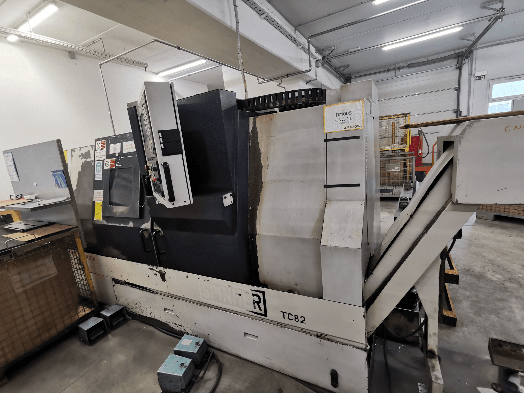 Maszyna CNC, marka Spinner, model TC82, widok z boku pokazujący panel sterowania i rynnę do usuwania złomu w warunkach warsztatowych.