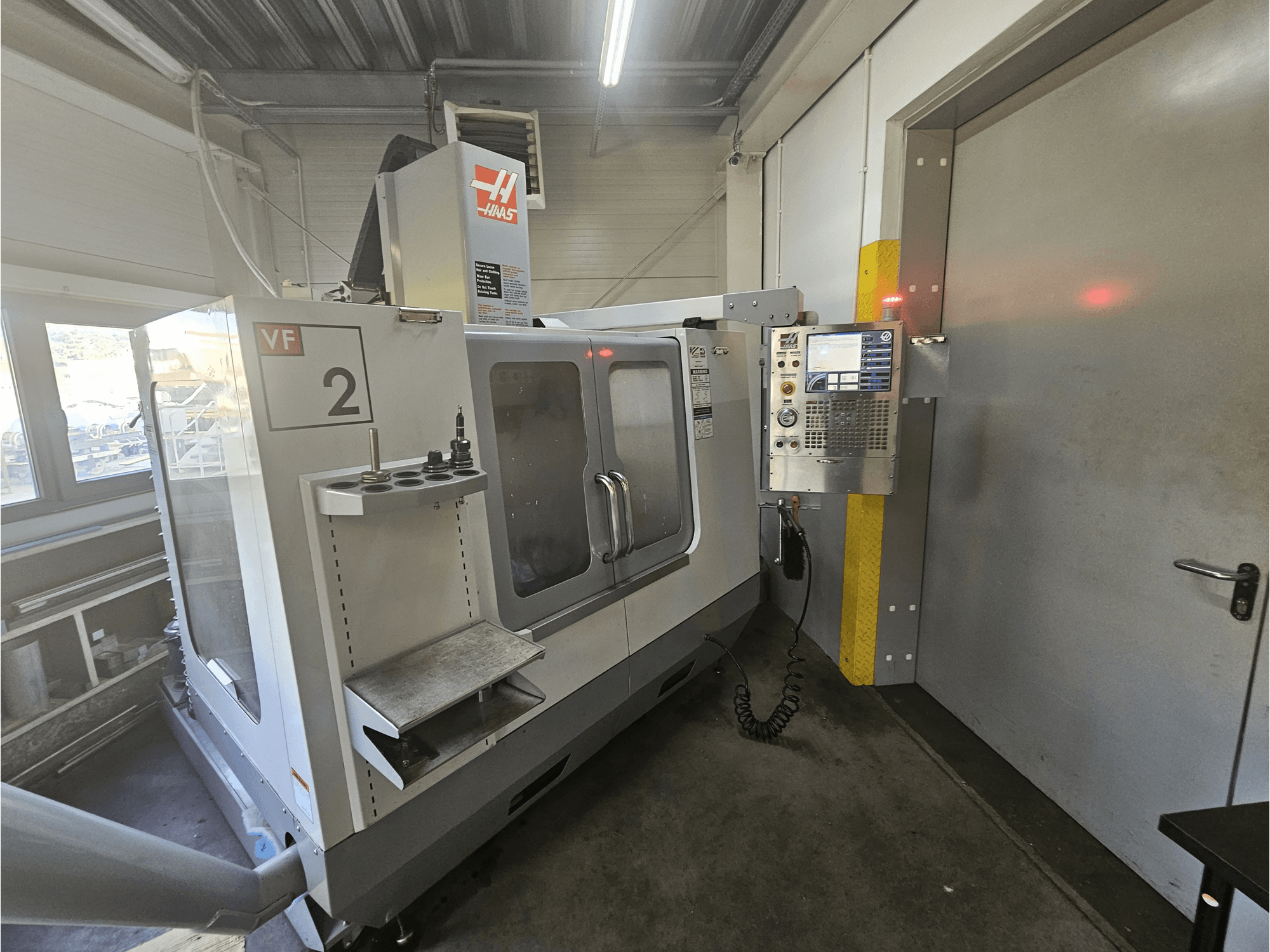 Frezarka CNC Haas VF-2, widok z przodu, pokazujący panel sterowania, uchwyty narzędziowe i przezroczyste okno w obszarze roboczym.