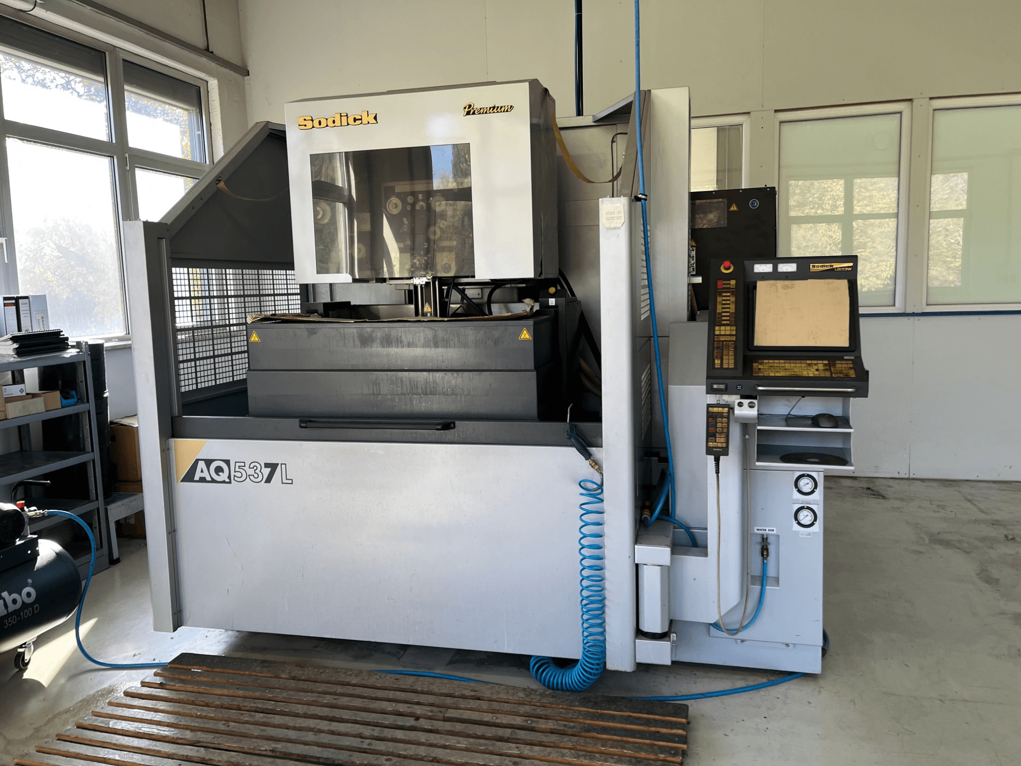 Maszyna elektroerozyjna (EDM) Sodick AQ537L w widoku z przodu, z panelem sterowania, przewodami chłodzenia wodą i przestrzenią roboczą.