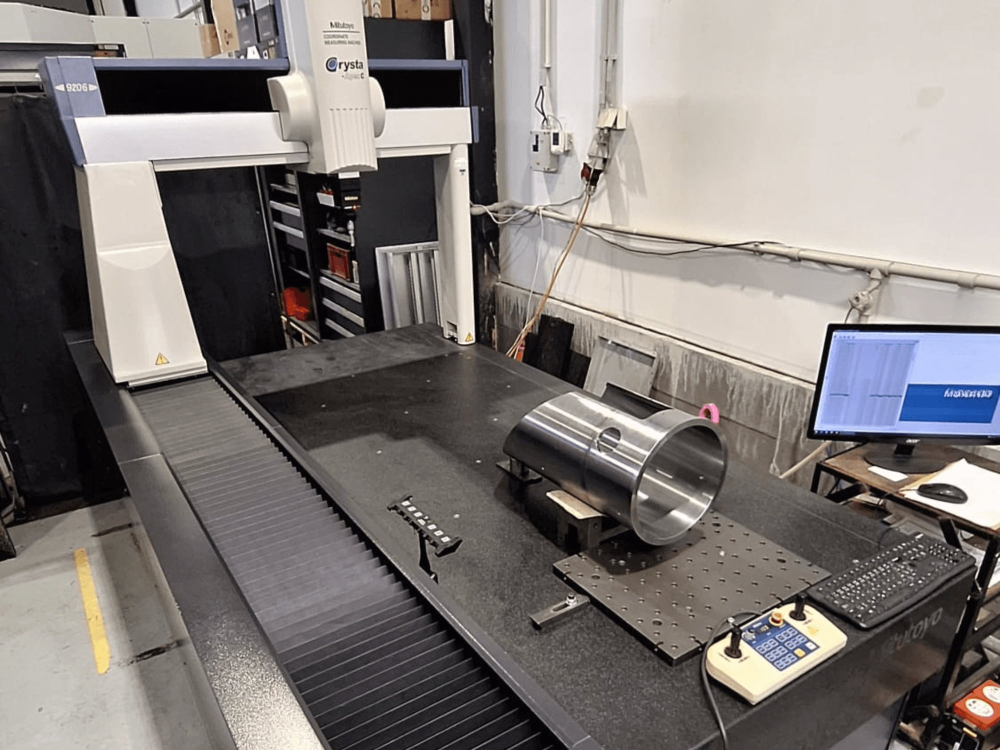 Współrzędnościowa maszyna pomiarowa Mitutoyo Crysta-Apex C9206 w widoku z przodu, mierząca cylindryczną część metalową na płycie z czarnego granitu.