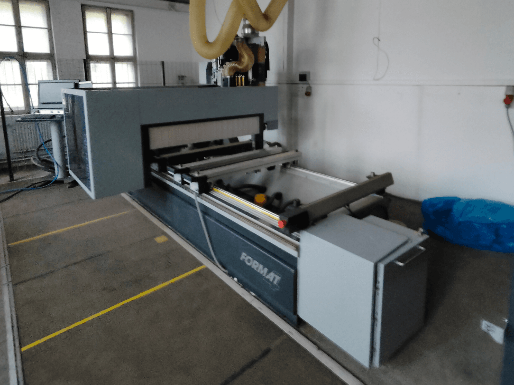 Widok z przodu maszyny CNC Format z szarym korpusem, szynami prowadzącymi i widocznym panelem sterowania.