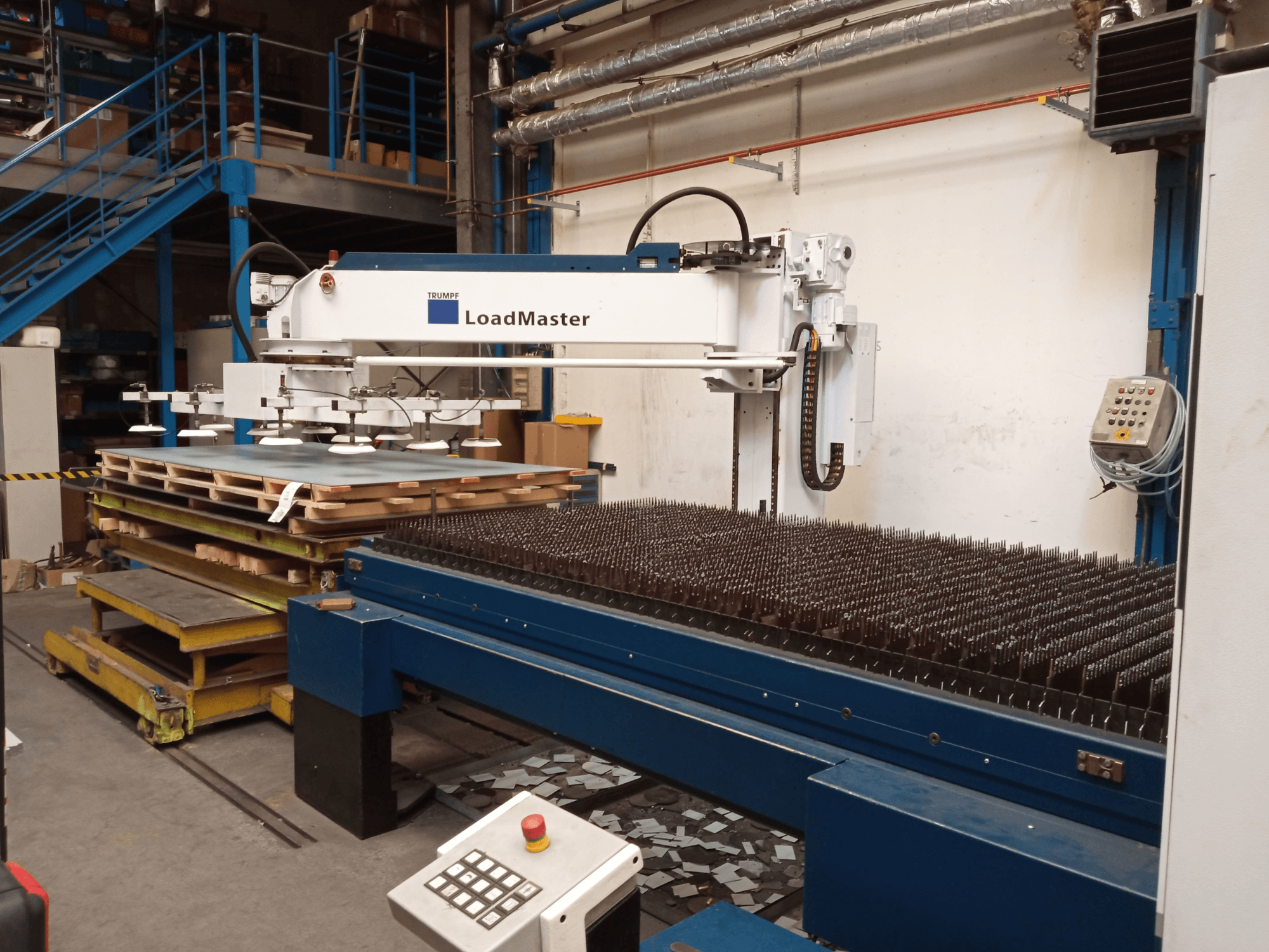 Maszyna do cięcia laserowego CO₂ TRUMPF TruLaser 3030 widziana z boku, wyposażona w system LoadMaster i palety z materiałami.