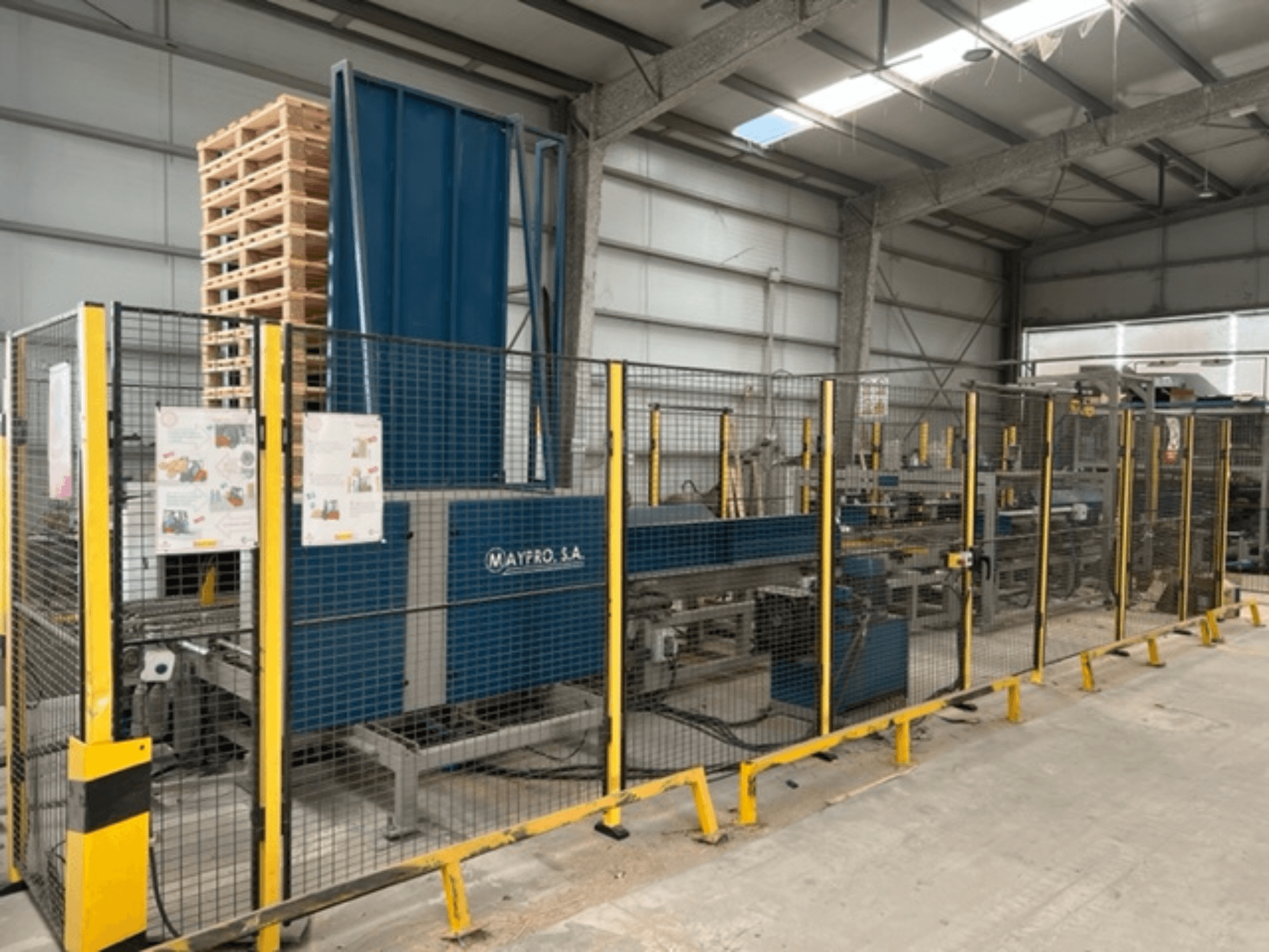 Przemysłowa maszyna do pakowania palet firmy Maypro S.A. w magazynie, wyposażona w siatkę zabezpieczającą i elementy sterujące, widok z boku.