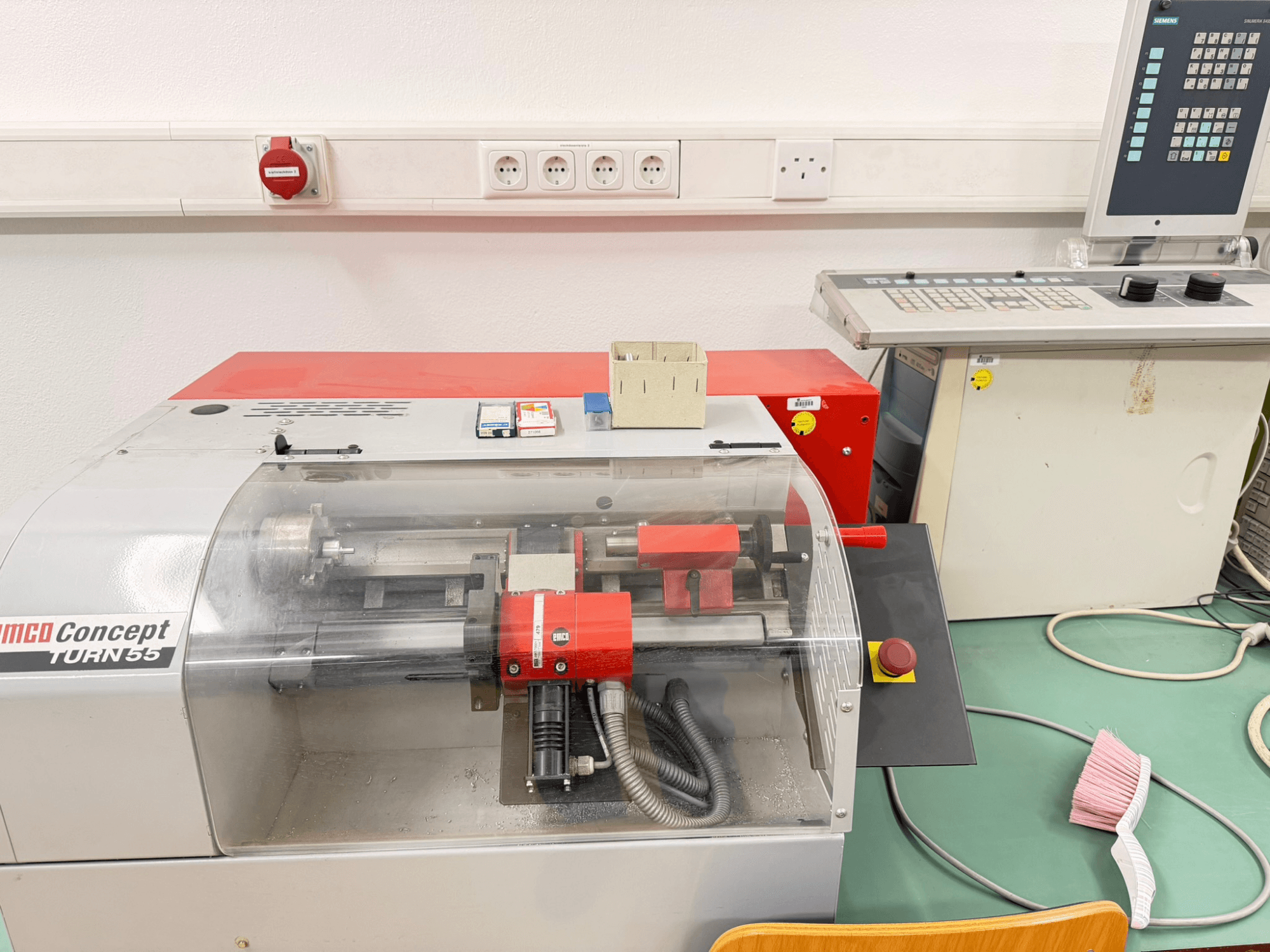 Obracarka pozioma EMCO Concept Turn 55 z czerwono-szarą obudową, widok z przodu przedstawiający elementy sterujące i obszar roboczy.