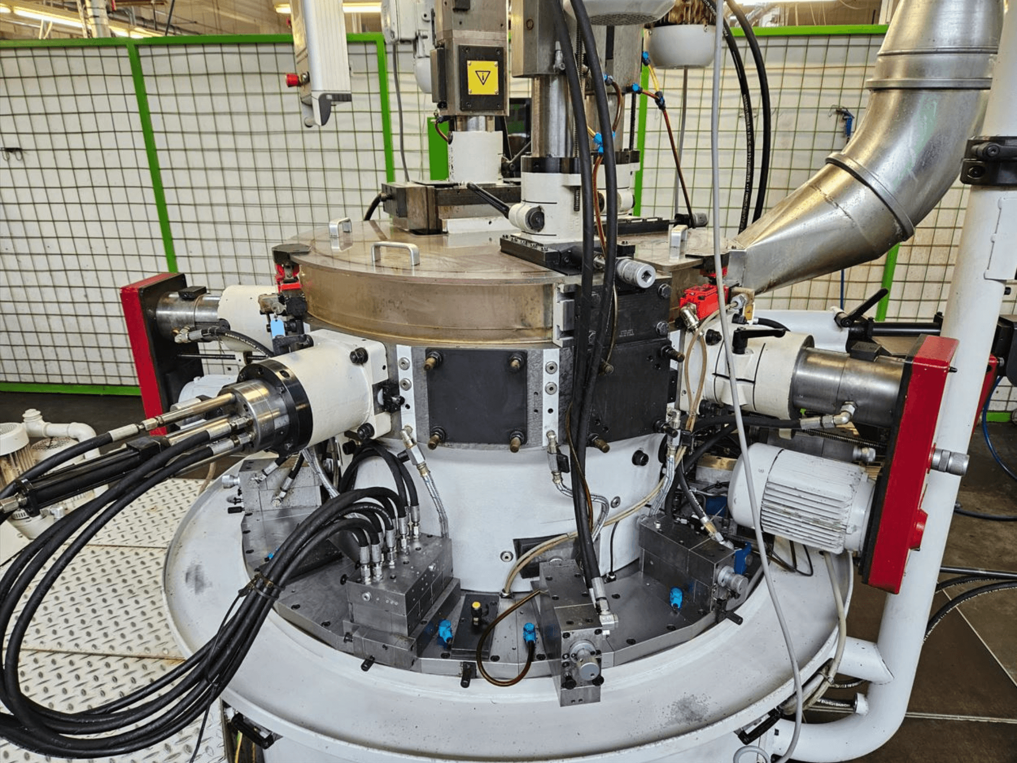 Zbliżenie na maszynę przemysłową z wężami hydraulicznymi, metalowymi elementami i obrotową podstawą. Nie widać marki.