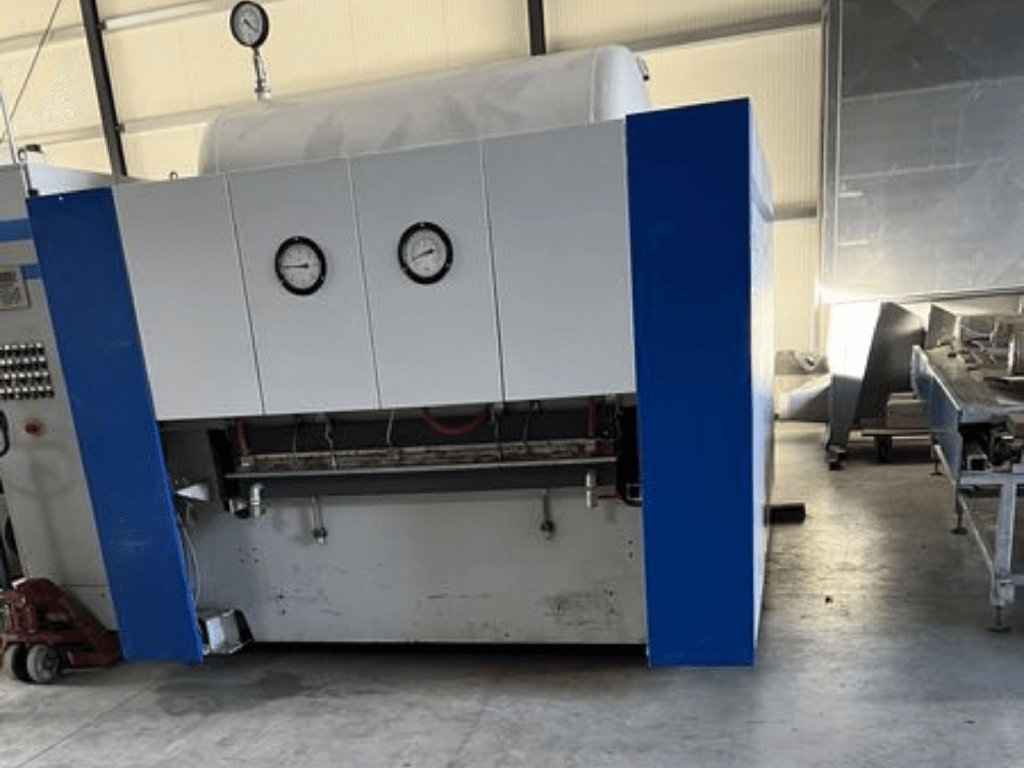 Niebiesko-biała maszyna przemysłowa z dwoma manometrami, widok z przodu, z panelem sterowania i przyległym sprzętem.
