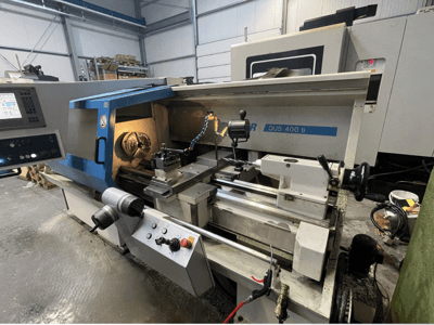 Tokarka CNC DUS 400 ti w widoku z przodu, z panelem sterowania, uchwytem narzędziowym i podświetlanym obszarem roboczym.