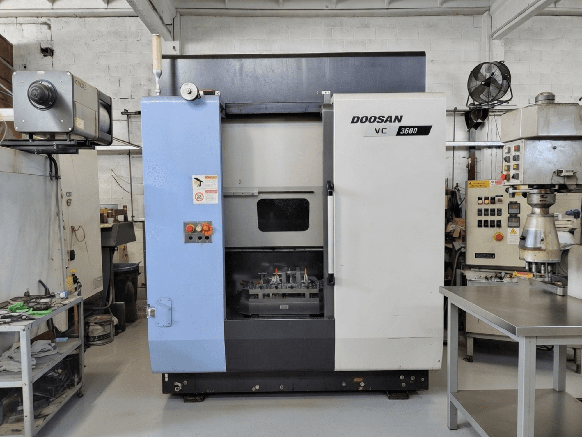 Pionowe centrum obróbcze DOOSAN VC 3600 w widoku z przodu, z panelem sterowania i otwartymi drzwiami odsłaniającymi przestrzeń roboczą.