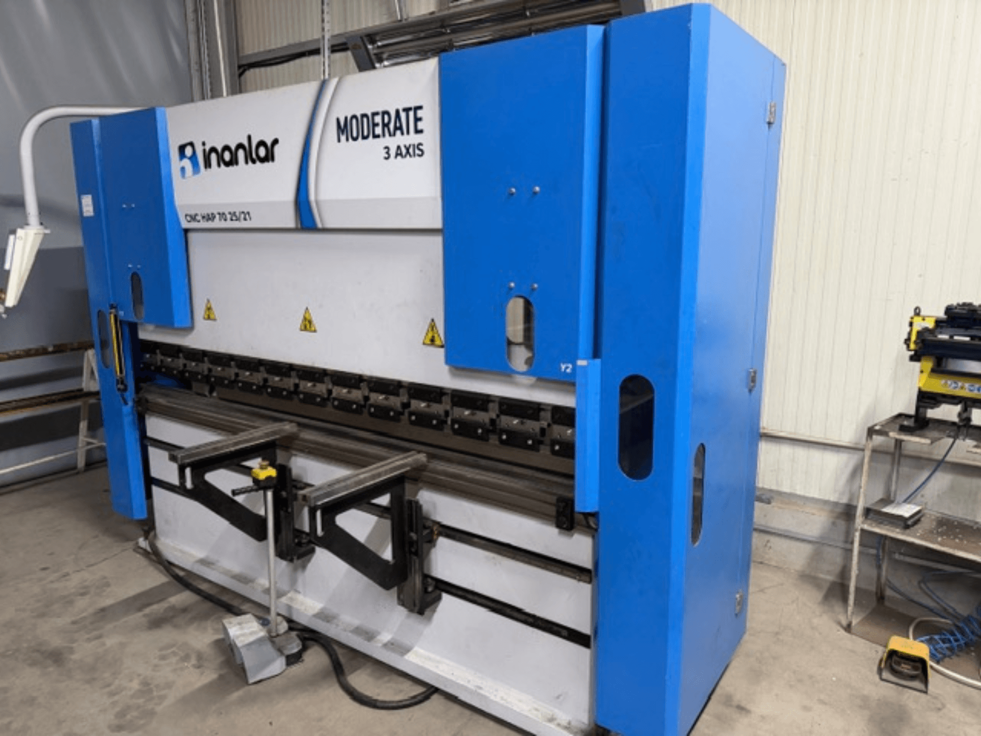 Inanlar Moderate 3-osiowa maszyna CNC w kolorze niebieskim, widok z przodu, posiada dźwignie sterujące i etykiety bezpieczeństwa widoczne na korpusie.