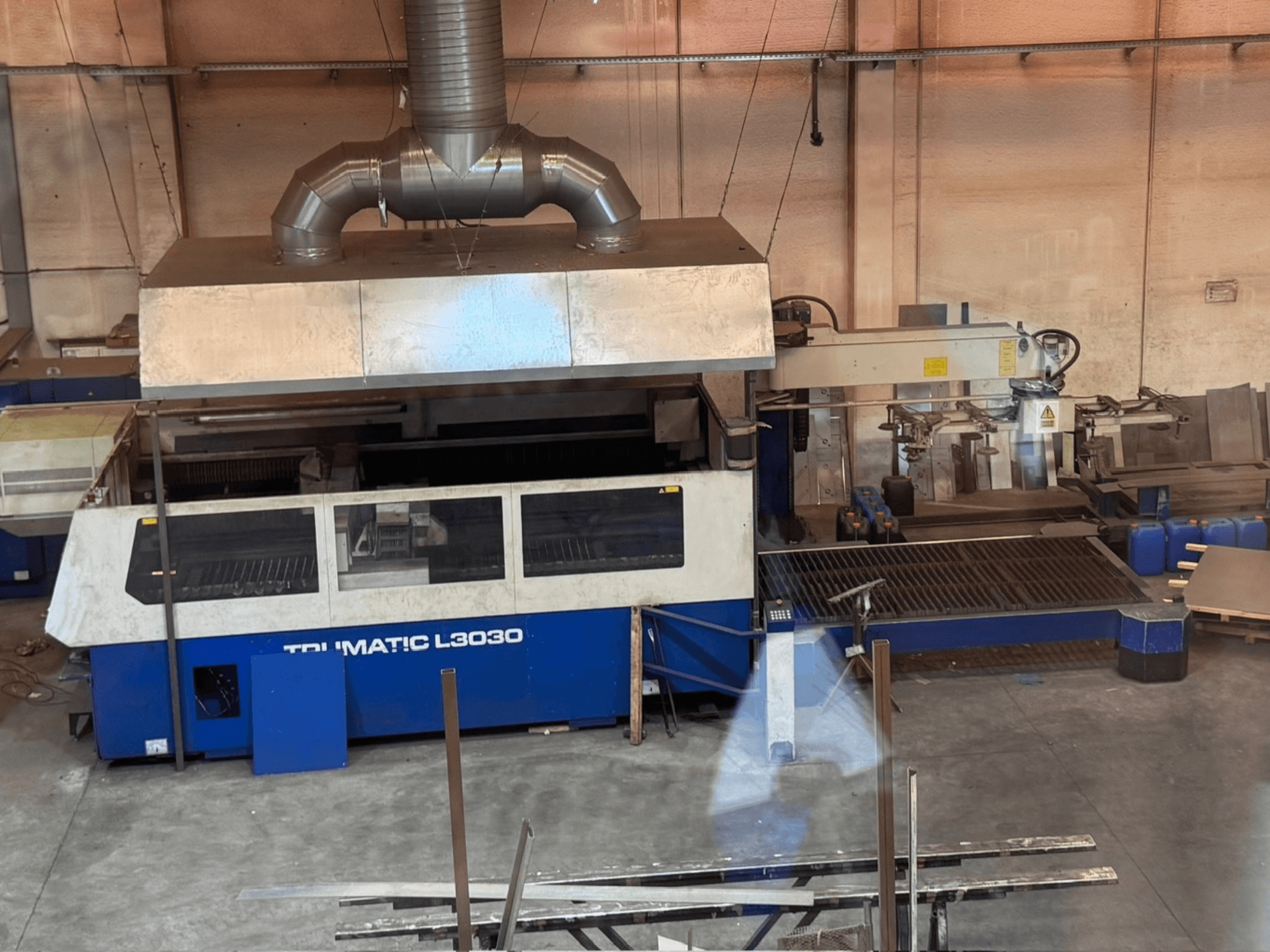 Maszyna do cięcia laserowego CO₂ TRUMPF TRUMATIC L3030 w warsztacie – widok z przodu przedstawiający panel sterowania i stół roboczy.