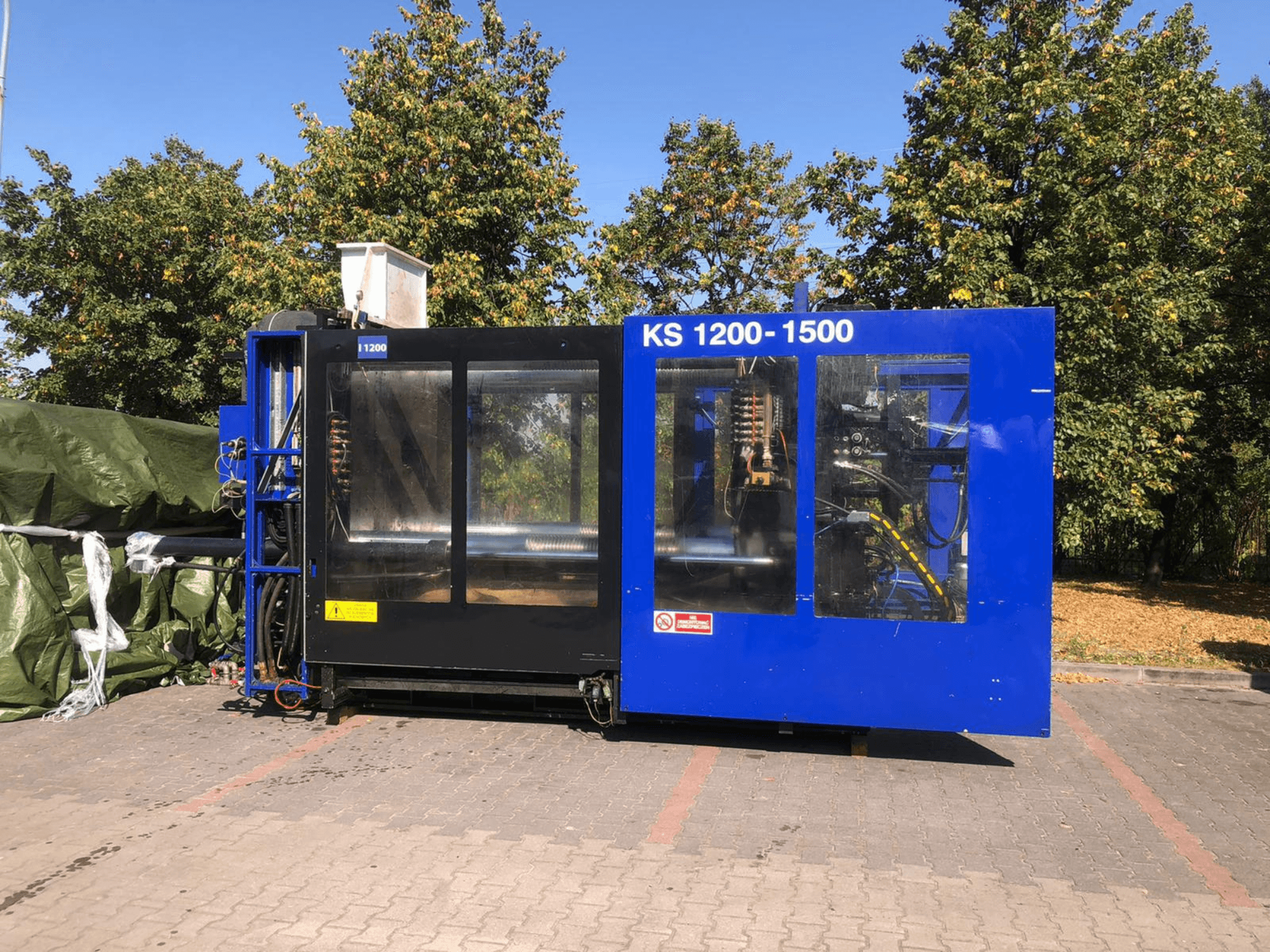 Hydrauliczna wtryskarka ITALTECH KS 1200 8300 ES, widok z boku, pokazująca elementy sterujące i szczegóły maszyny w otoczeniu parku.