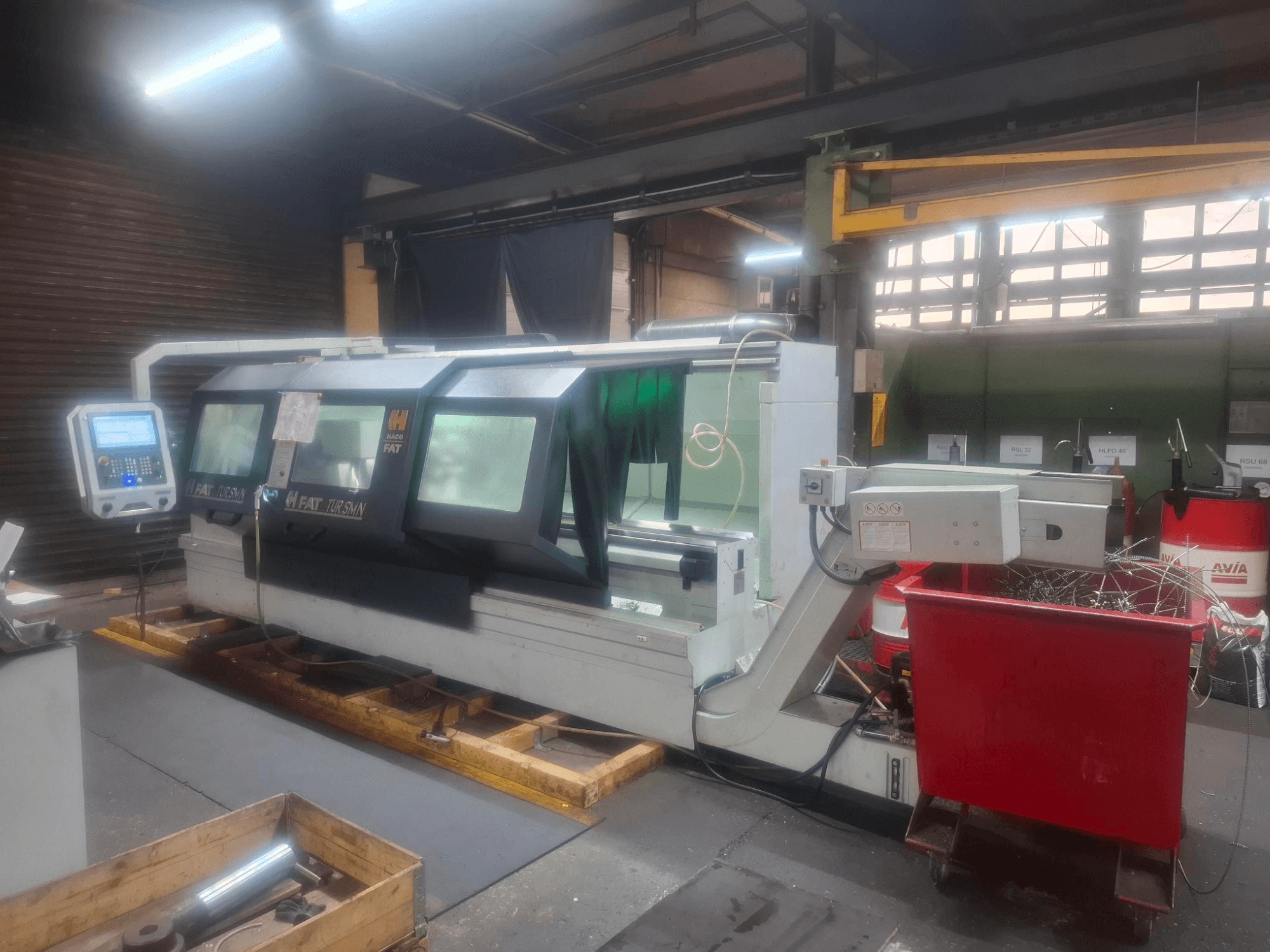 Widok z przodu maszyny CNC FAT Tursan z panelem sterowania, umieszczonej na drewnianych paletach w warsztacie.