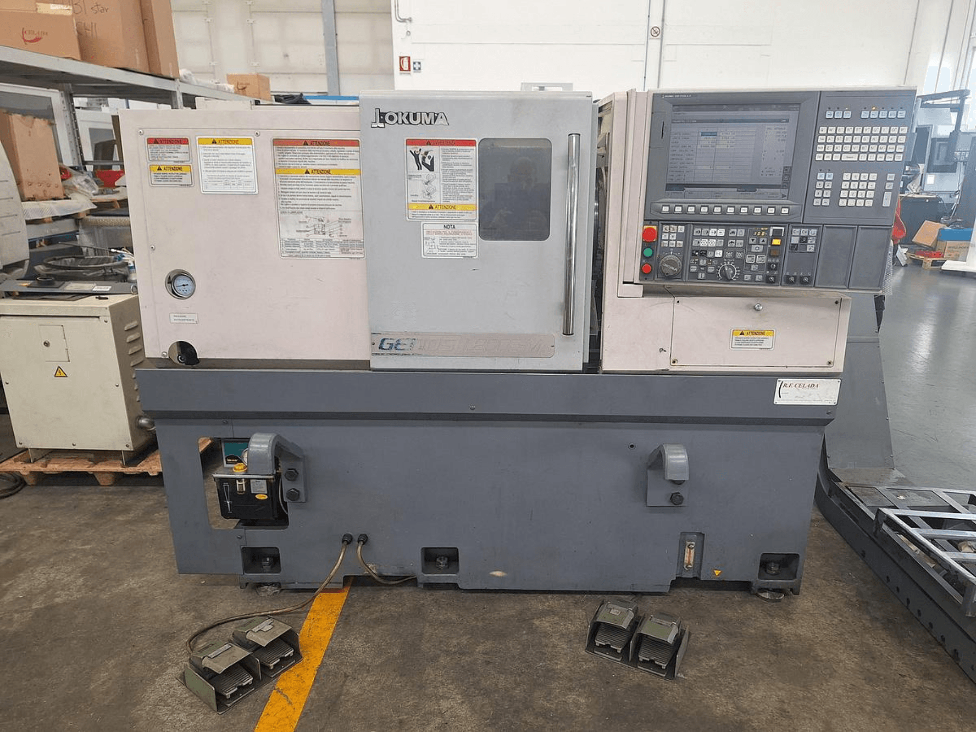 Okuma GENOS L200E-M tokarka pozioma w widoku z boku; posiada panel sterowania, ostrzeżenia bezpieczeństwa i pedały nożne.