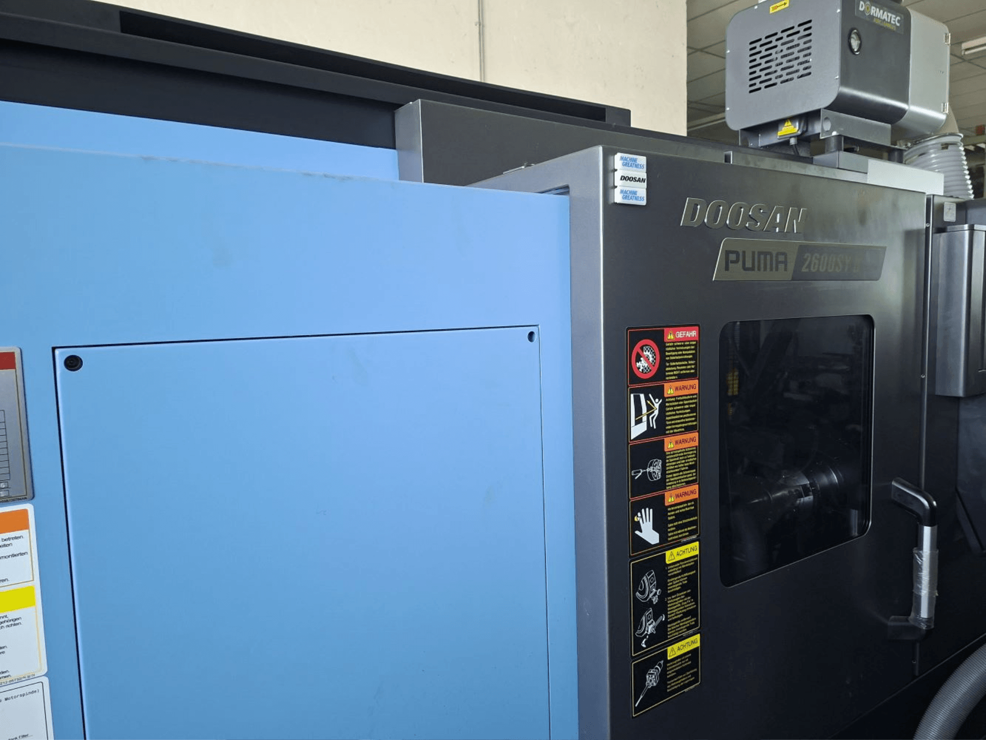 Obracarka pozioma DOOSAN PUMA 2600 SY II, widok z przodu, etykiety bezpieczeństwa i niebieskie panele.