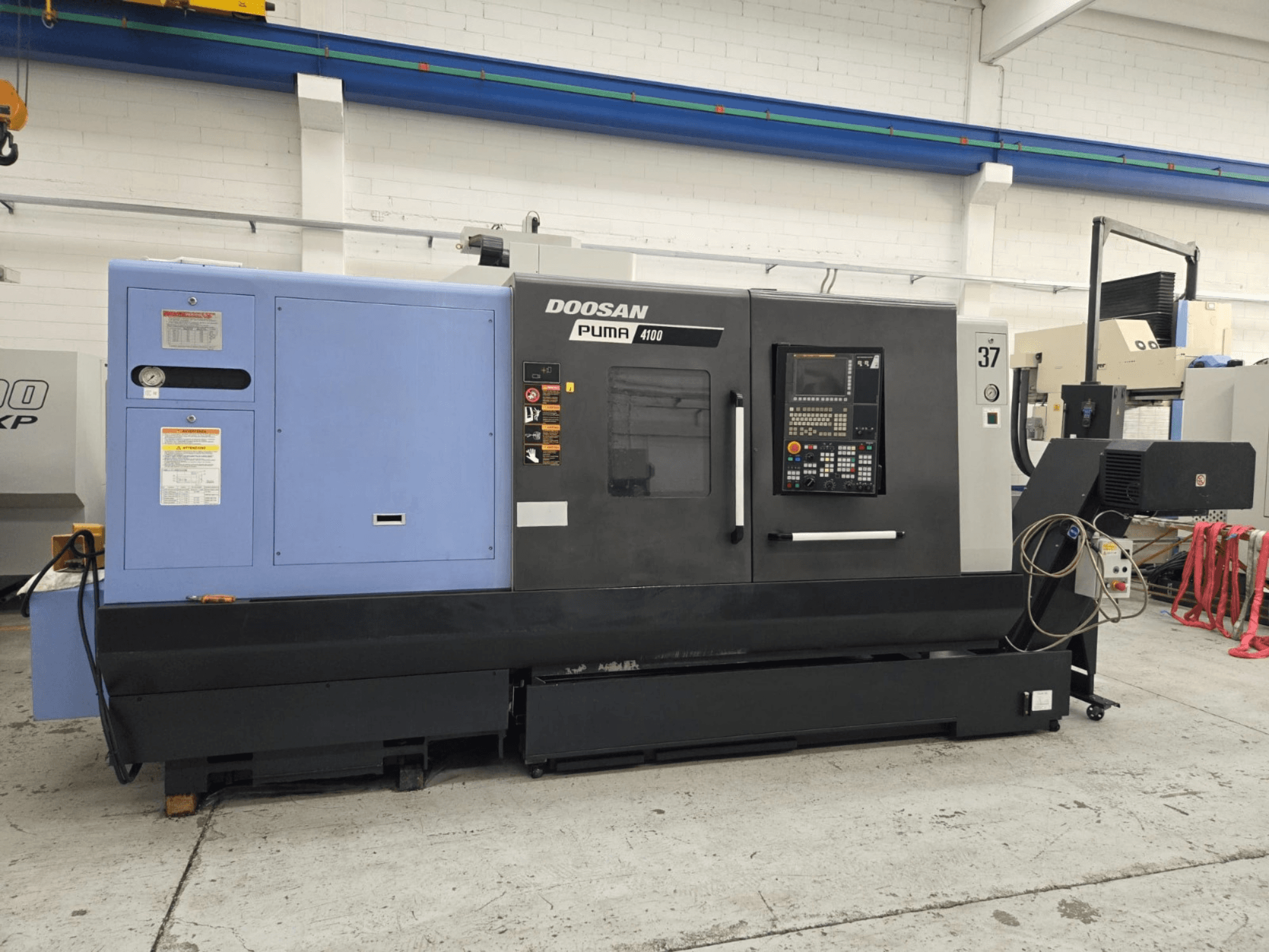 Tokarka CNC Doosan Puma 4100, widok z przodu; posiada panel sterowania, niebieską jednostkę zasilającą i szczegółowe etykiety zawierające wskazówki dotyczące obsługi.
