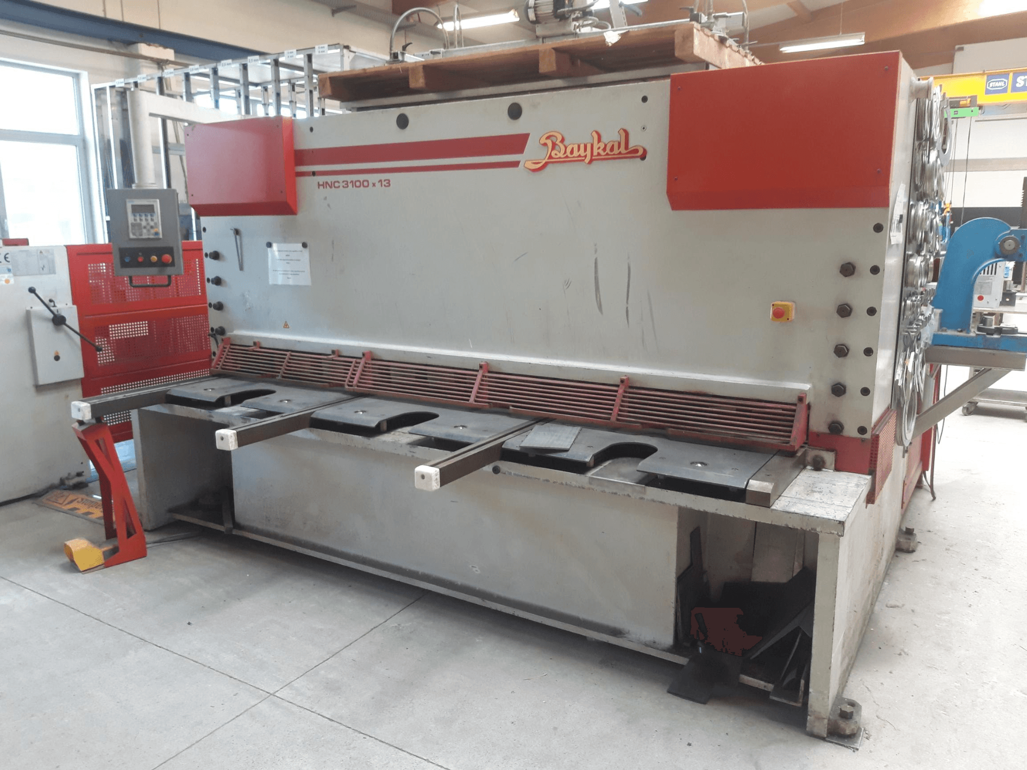 Widok z przodu nożyc CNC Baykal HNC 3100x13, przedstawiający panel sterowania, obszar cięcia metalu oraz miejsce na zbieranie odpadów.