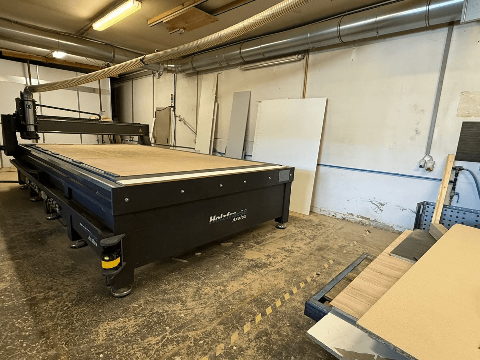 Frezarka CNC Holz-Her Axos 5 w warsztacie, widok z przodu przedstawiający stół roboczy, system odsysania pyłu i drewniane panele w pobliżu.