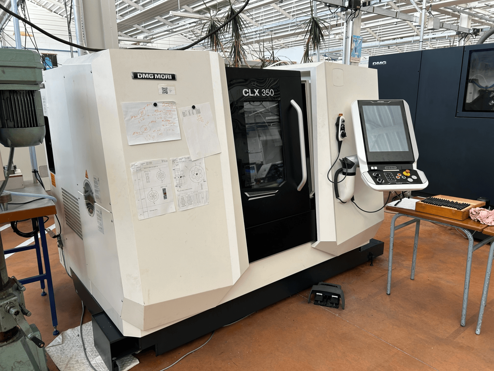 Pozioma tokarka DMG MORI CLX 350 V4, widok z przodu wraz z panelem sterowania i załączoną dokumentacją techniczną.