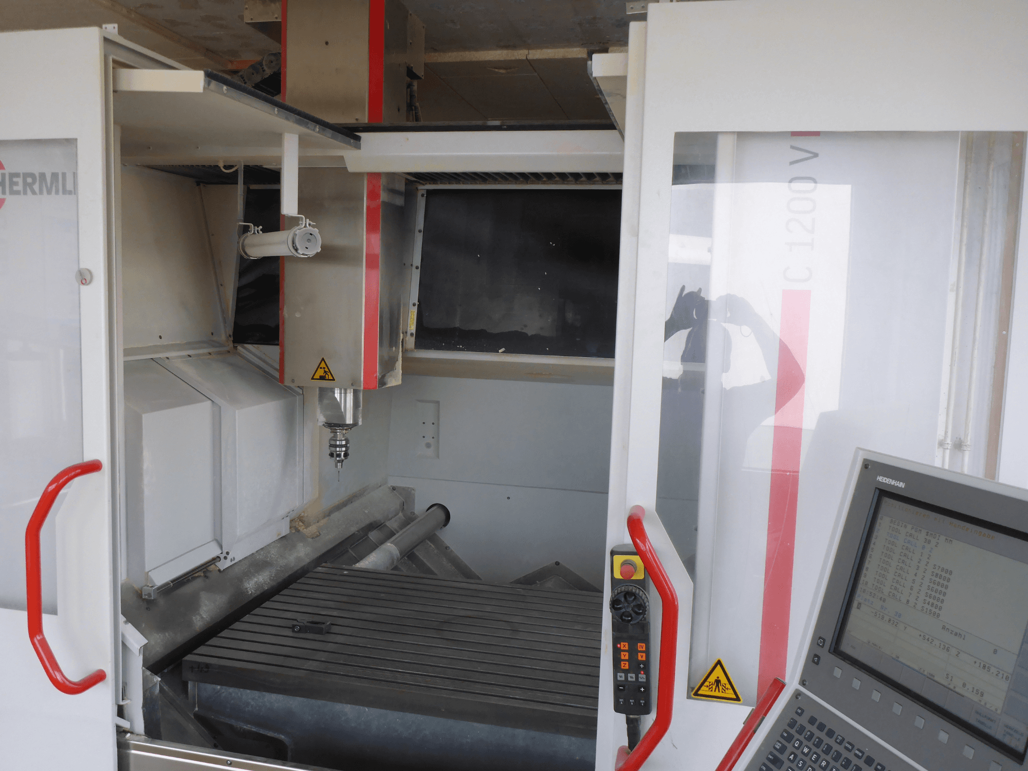 Wnętrze pionowego centrum obróbczego HERMLE C 1200 z uchwytem narzędziowym, panelem sterowania i stołem roboczym w widoku z przodu.