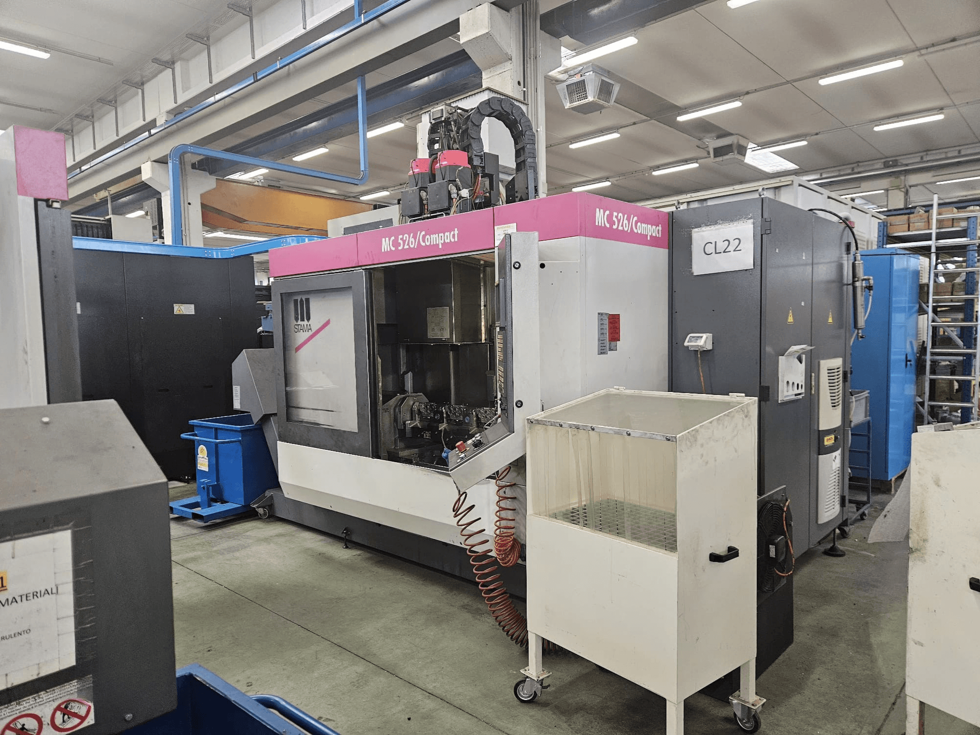 MC 526 Kompaktowa maszyna CNC firmy Stama, widok z boku, pokazujący panel sterowania, zbiornik chłodziwa i sąsiednie maszyny.