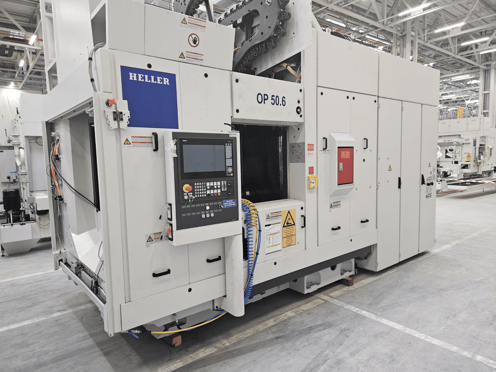 Centrum obróbcze Heller OP 50.6, widok z przodu, z panelem sterowania, etykietami ostrzegawczymi i wężami widocznymi w ustawieniu fabrycznym.