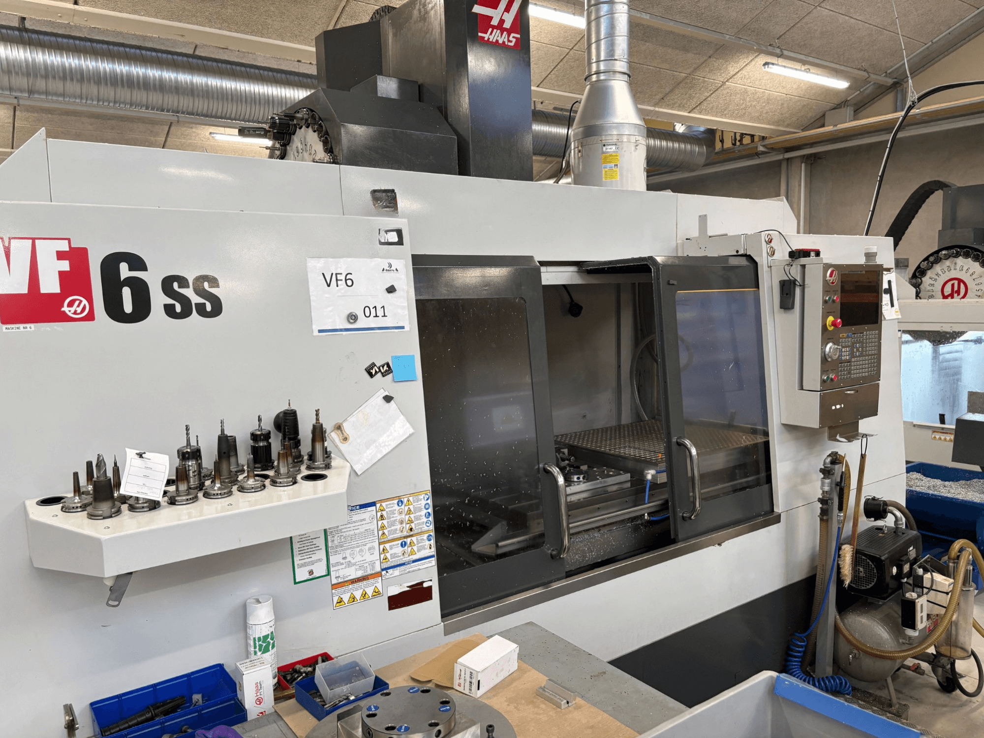 Frezarka CNC Haas VF-6 SS, widok z przodu. Zawiera różne narzędzia, panel sterowania i widoczny wewnętrzny obszar roboczy.