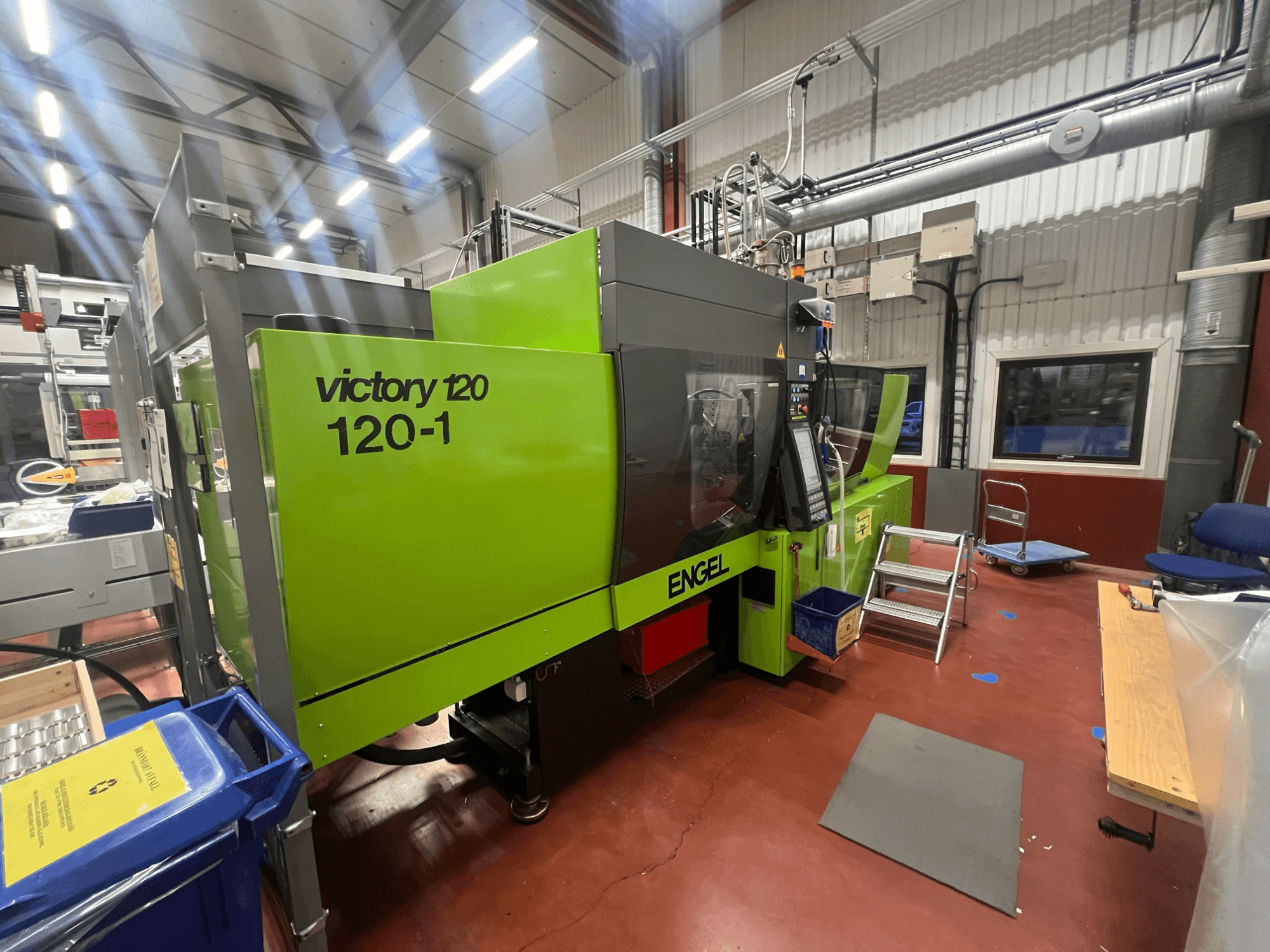 Zielona wtryskarka ENGEL Victory 120-1, widok z przodu, z panelem sterowania i stopniami, w warunkach przemysłowych.