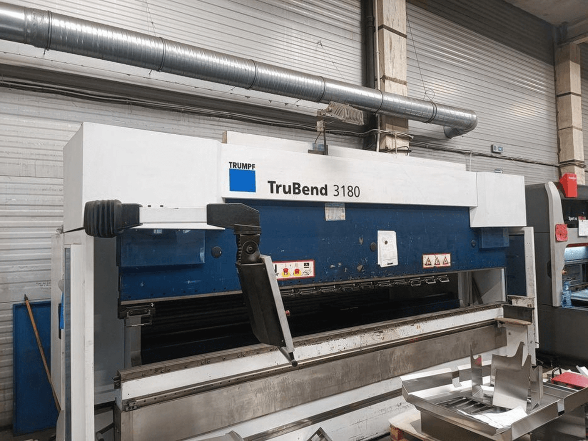 Giętarka Trumpf TruBend 3180 w warsztacie, widok z boku pokazujący panel sterowania i elementy metalowe na stole.