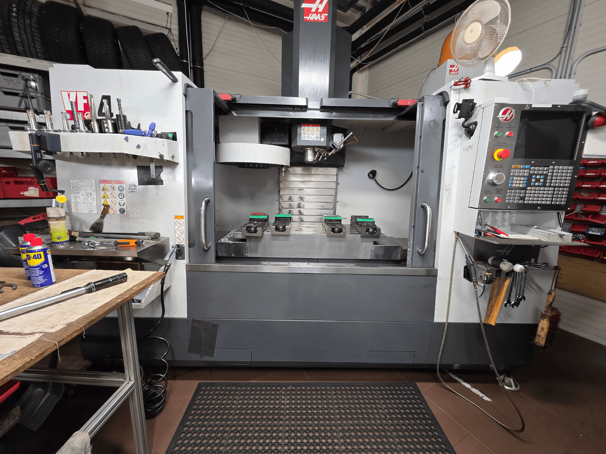 Widok z przodu frezarki CNC Haas VF-4 w warsztacie z narzędziami, interfejsem komputerowym i dwoma przedmiotami obrabianymi na stole.