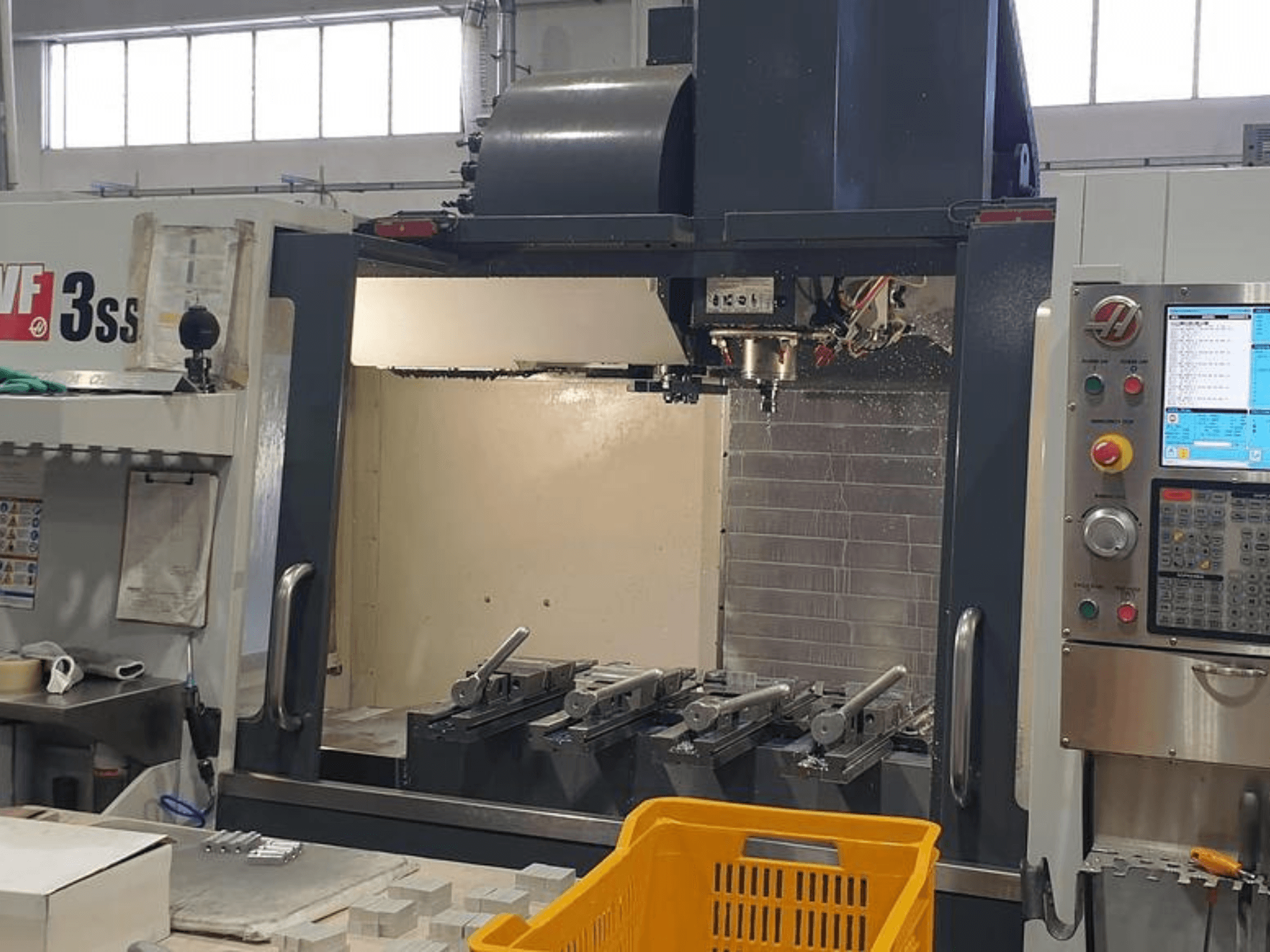 Pionowe centrum obróbcze HAAS VF-3SS, widok z przodu z panelem sterowania CNC, narzędziami i pomarańczowym koszem.