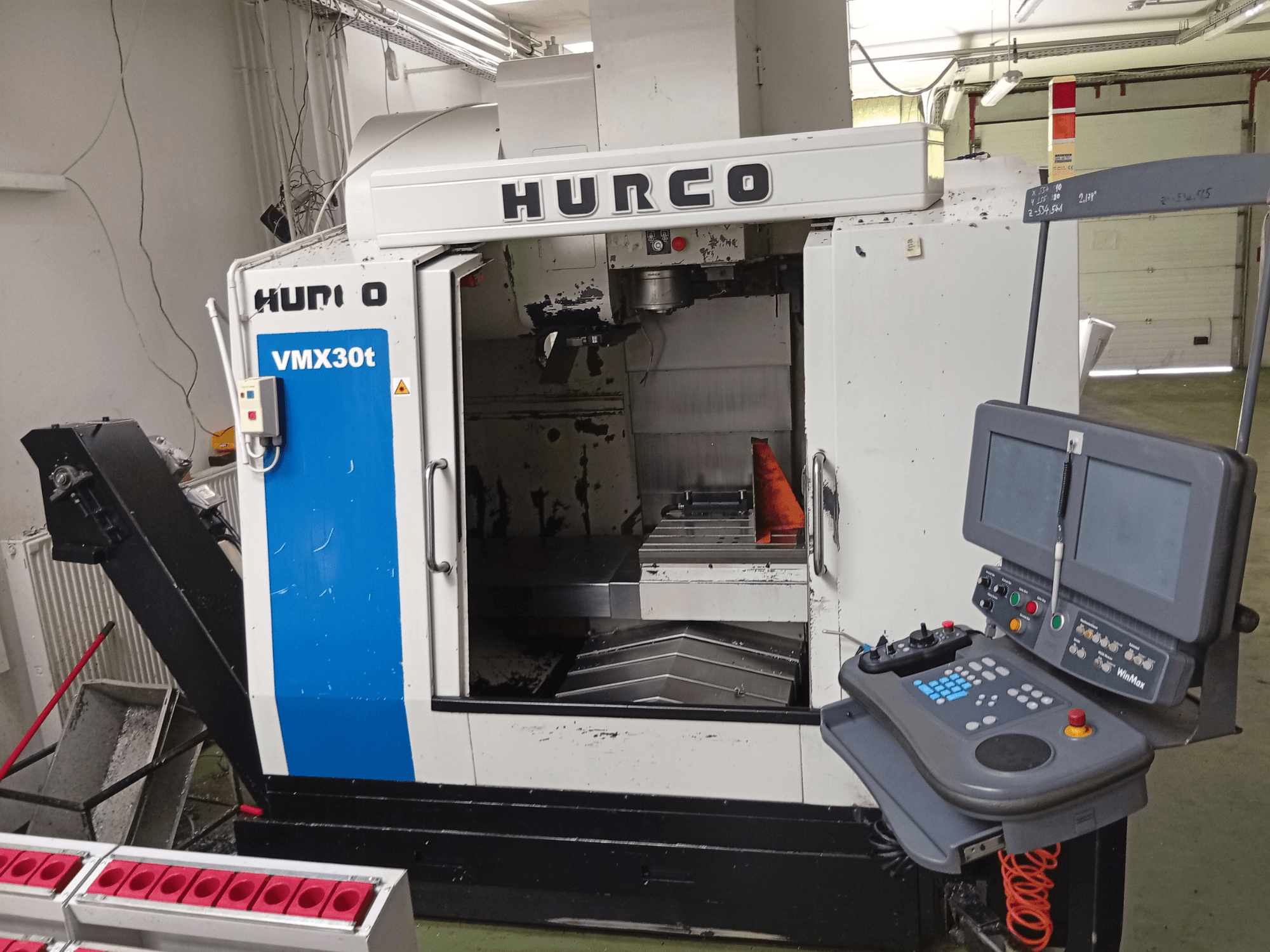 Pionowe centrum obróbcze Hurco VMX 30T, widok z przodu, przedstawiające panel sterowania i obszar wrzeciona wraz z widocznym stołem roboczym.