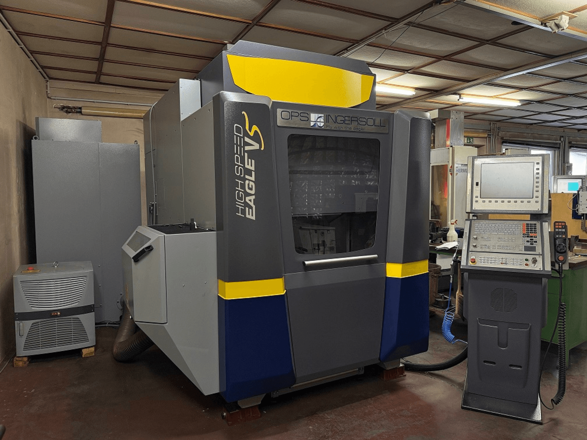 Szybkobieżna maszyna Eagle V firmy OPS Ingersoll, widok z boku, z panelem sterowania i przyległym sprzętem w otoczeniu przemysłowym.