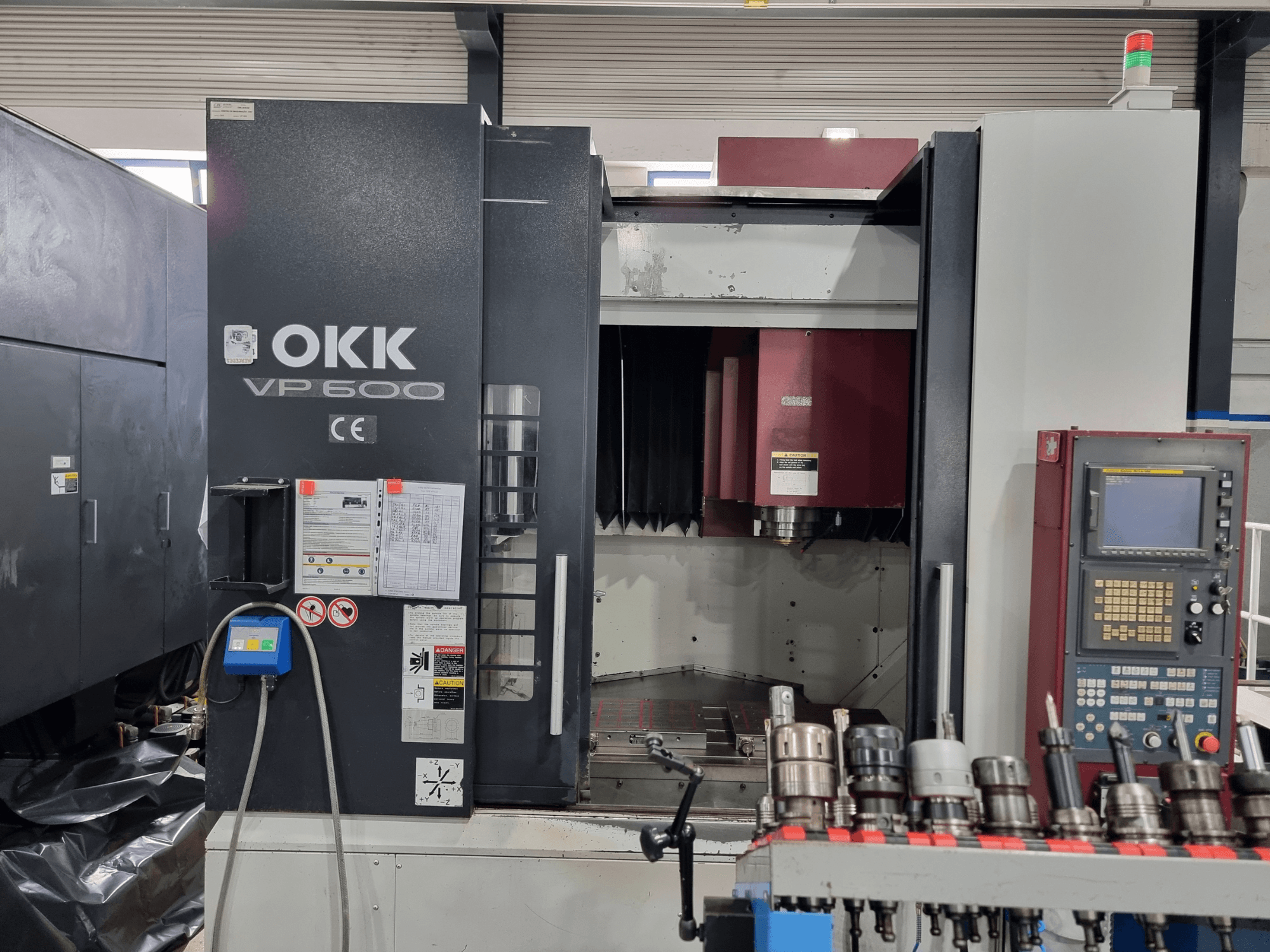 Pionowe centrum obróbcze OKK VP600 widziane z przodu, z widocznym panelem sterowania i uchwytami narzędziowymi na stojaku.