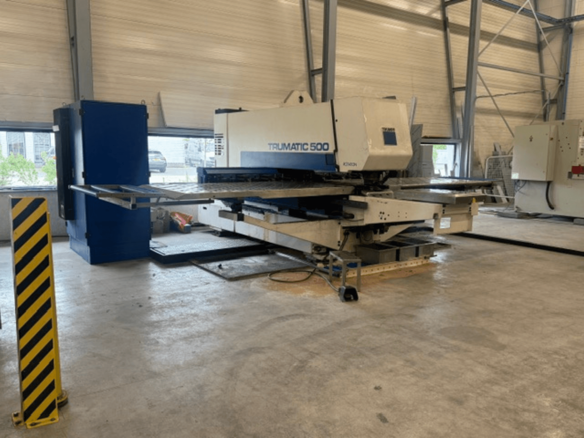 Wykrawarka CNC TRUMPF Trumatic 500 w warsztacie – widok z boku przedstawiający maszynę oraz słupek zabezpieczający z żółtymi paskami.