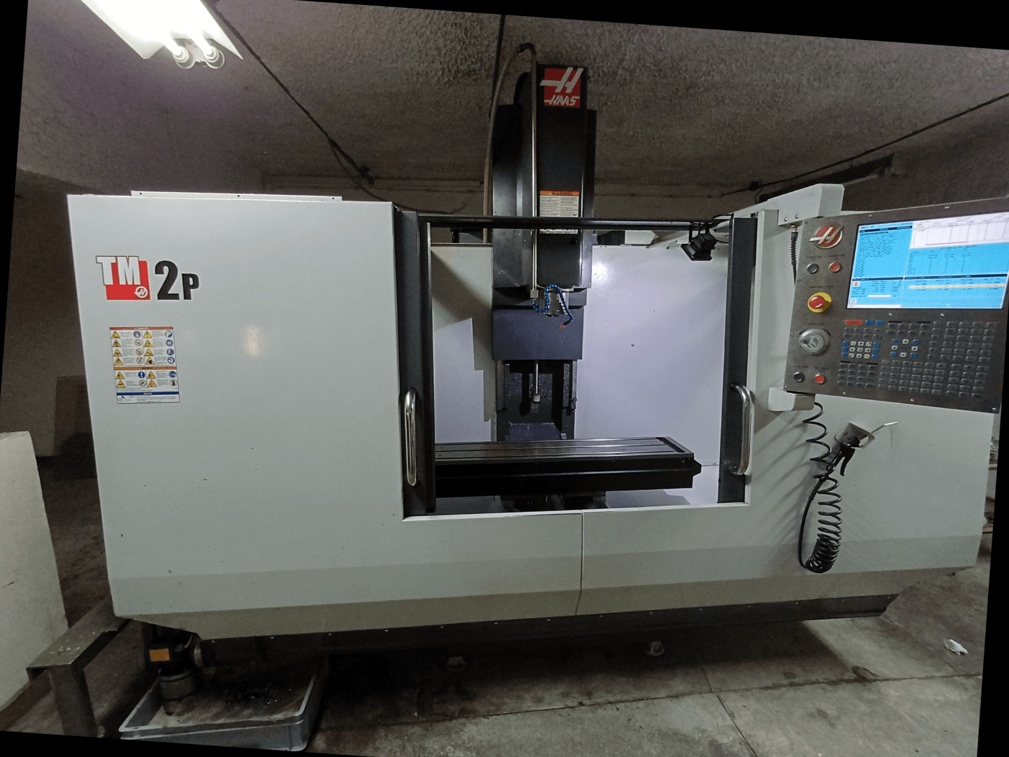 Pionowe centrum obróbcze HAAS TM-2P, widok z przodu, pokazujący panel sterowania, głowicę wrzeciona i łoże maszyny.