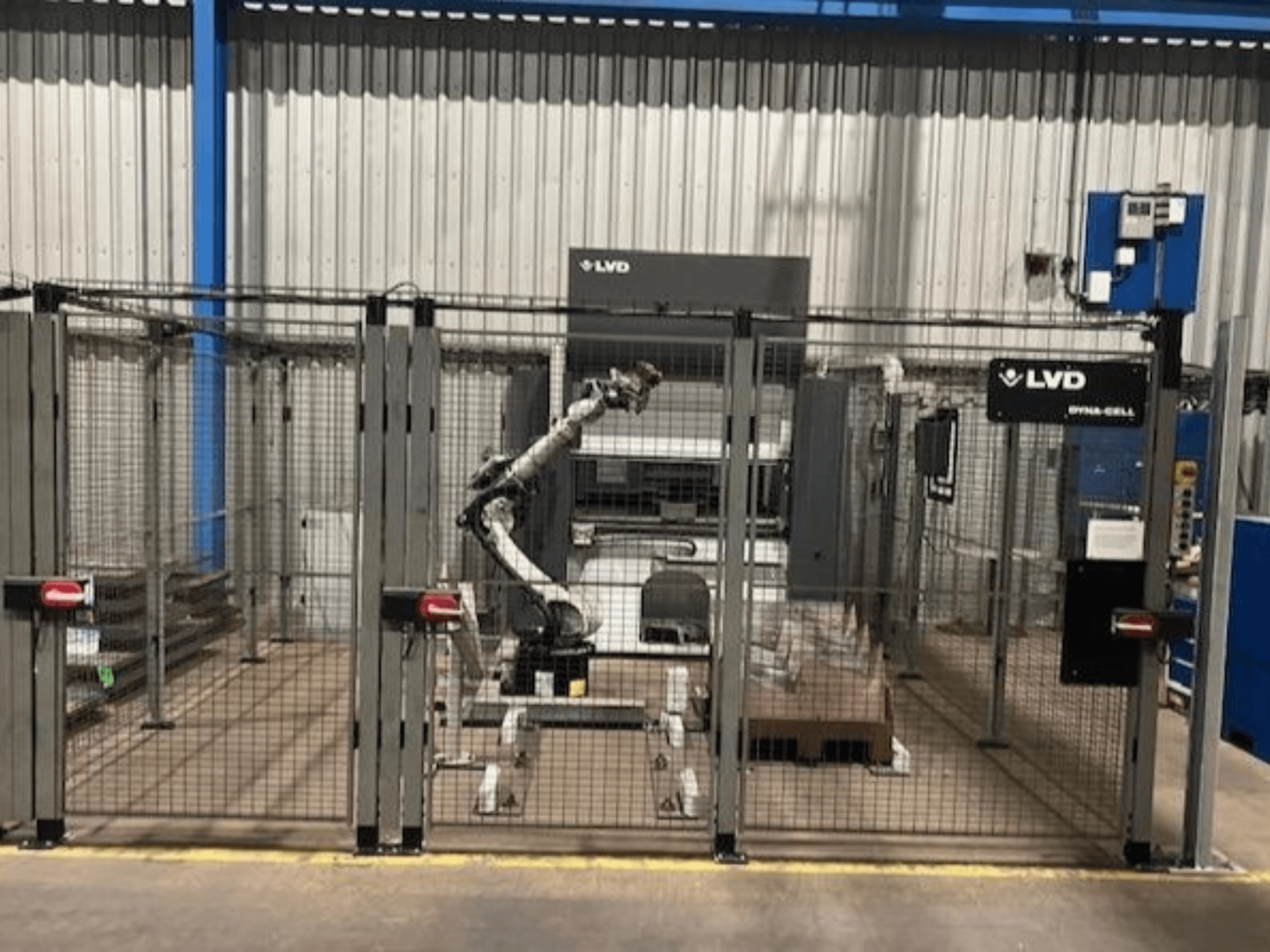 Zrobotyzowana stacja robocza LVD Dyna-Cell w ogrodzonej obudowie, widok z przodu, z ramieniem robota i panelem sterowania.