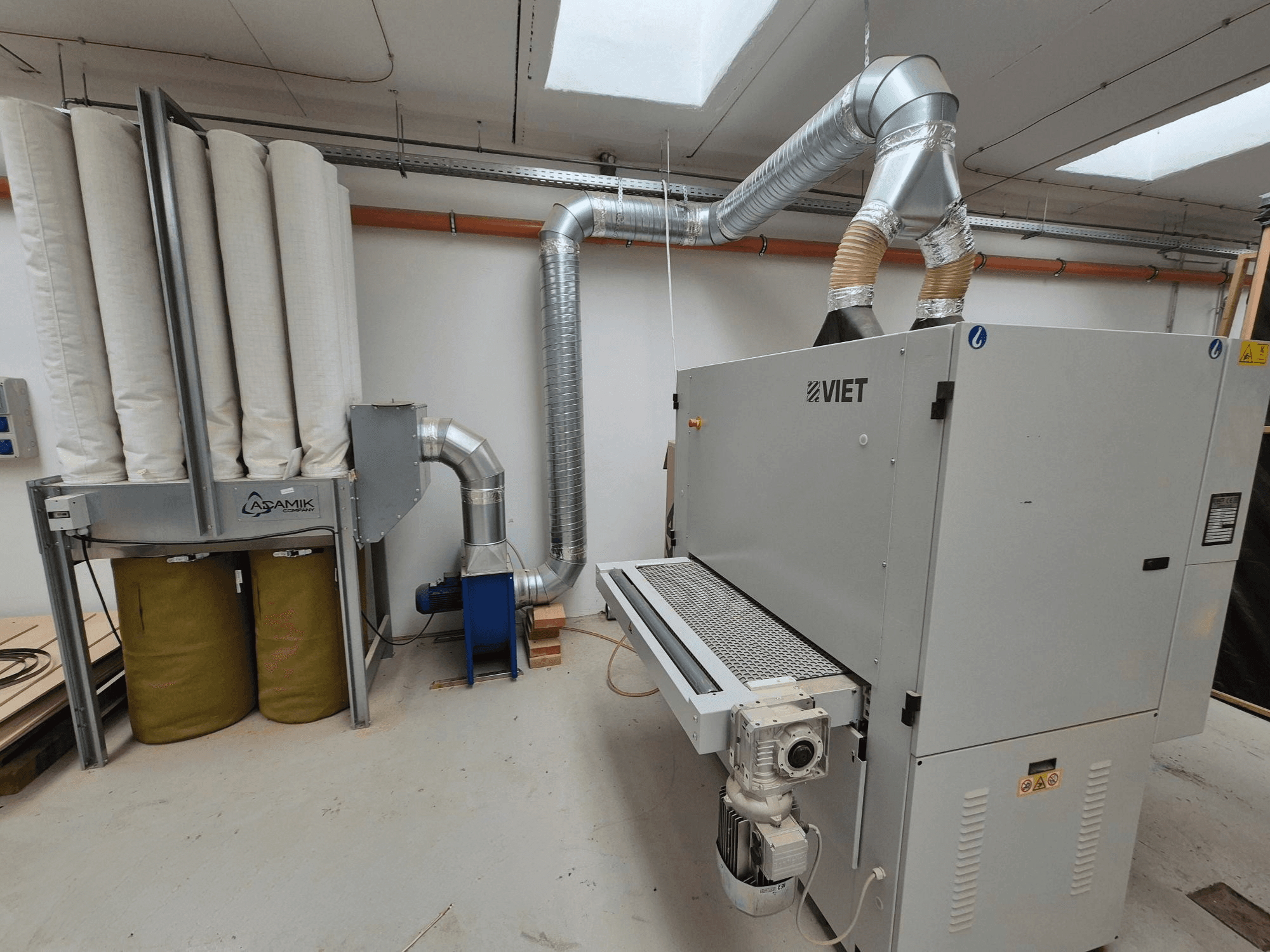 Wietnamski system odsysania pyłu z cylindrycznymi filtrami i srebrnym wylotem, widziany z przodu w warunkach warsztatowych.