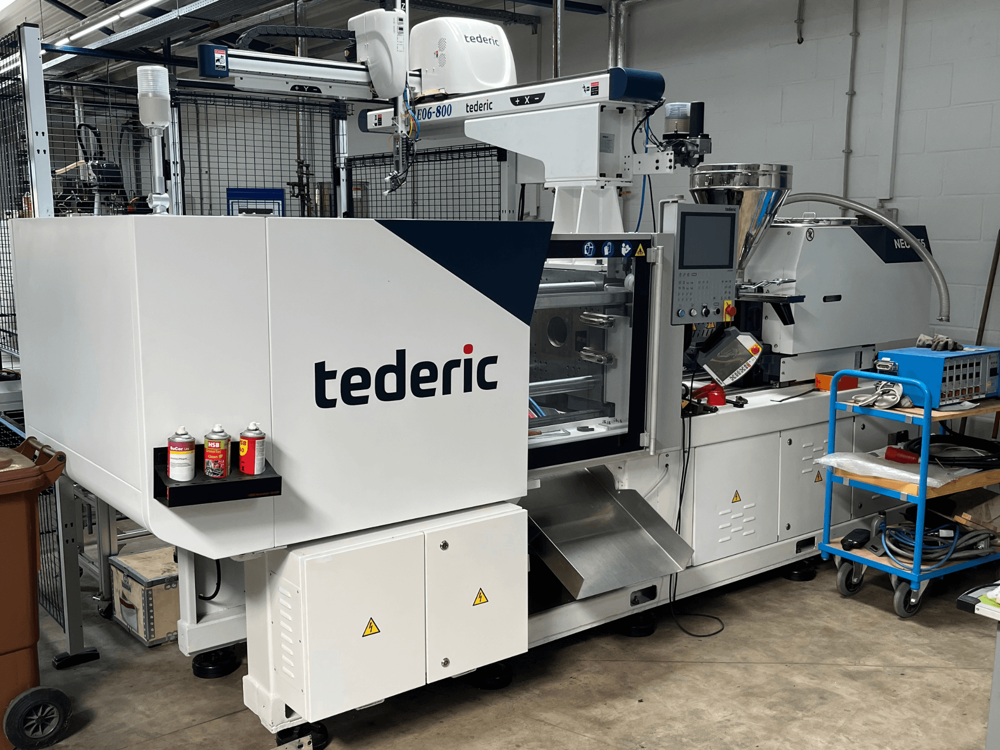 Hydrauliczna wtryskarka TEDERIC NEO.E55/e110h w warsztacie, widok z boku z panelem sterowania i sąsiednimi narzędziami.