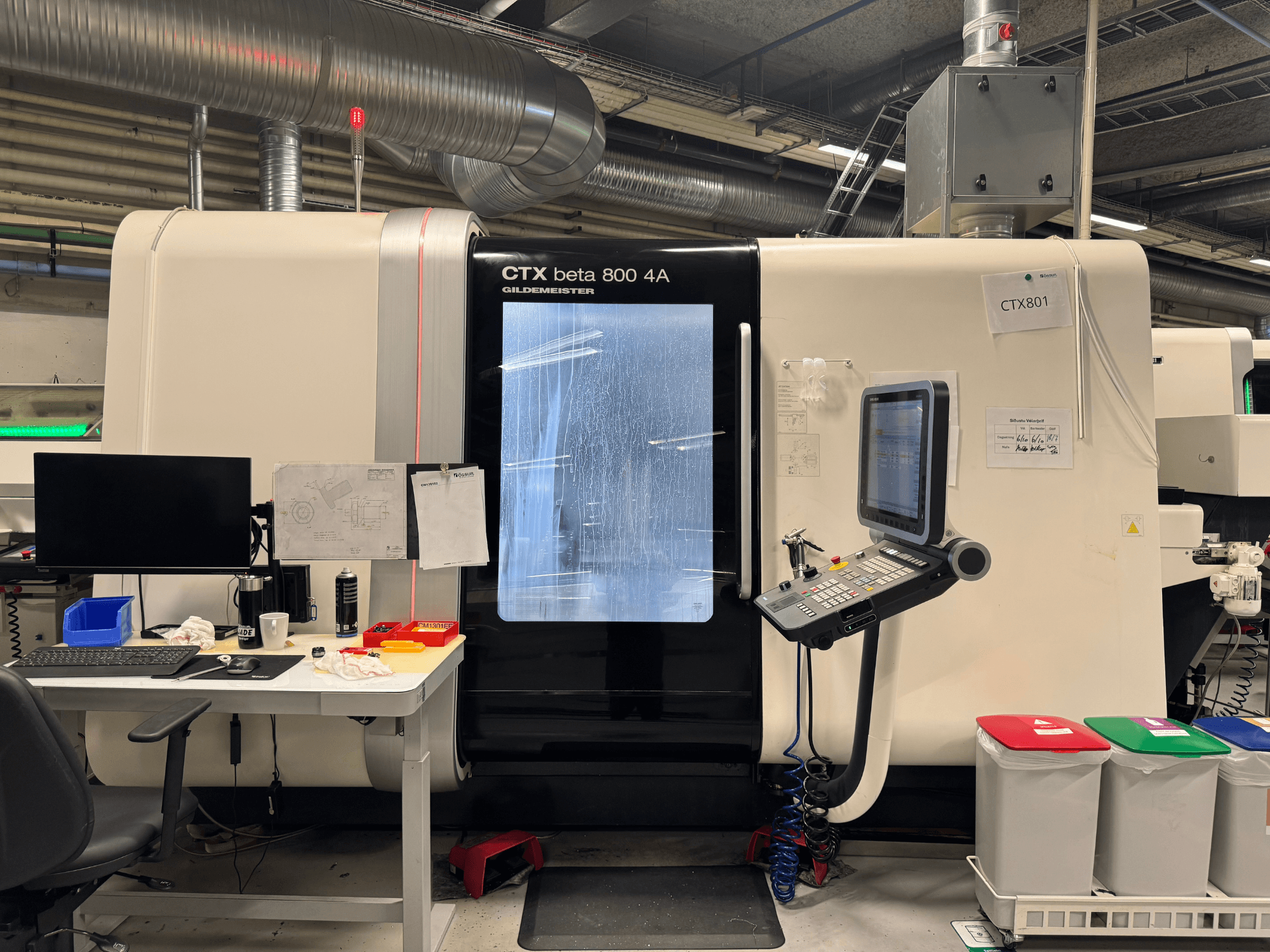 Maszyna CTX beta 800 4A z panelem sterowania i monitorem, widok z boku, w warsztacie z wyposażeniem biurowym i kolorowymi koszami na śmieci.