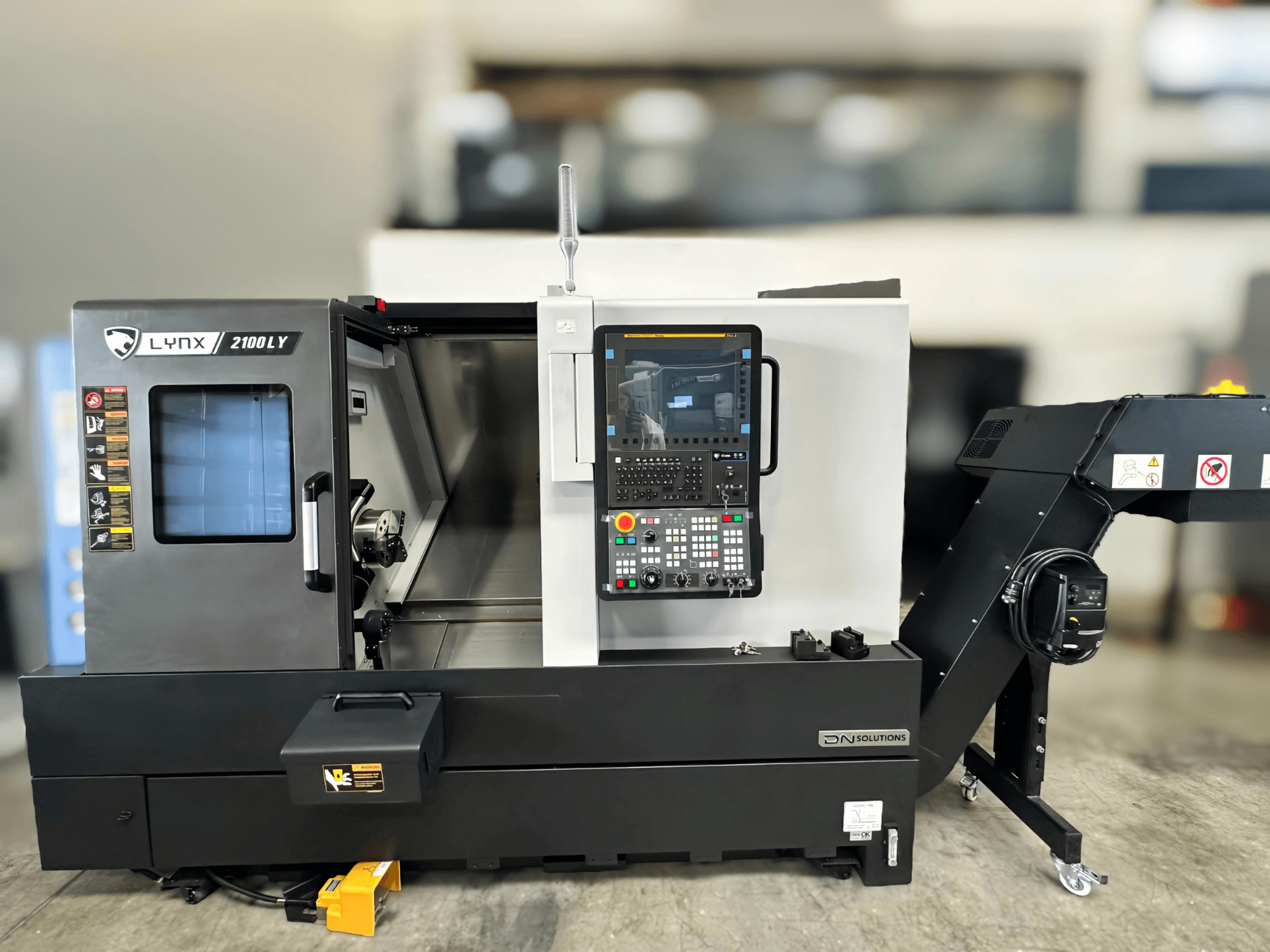 Tokarka pozioma DN SOLUTIONS LYNX 2100LYB, widok z przodu, z panelem sterowania i otwartymi drzwiami odsłaniającymi wnętrze.